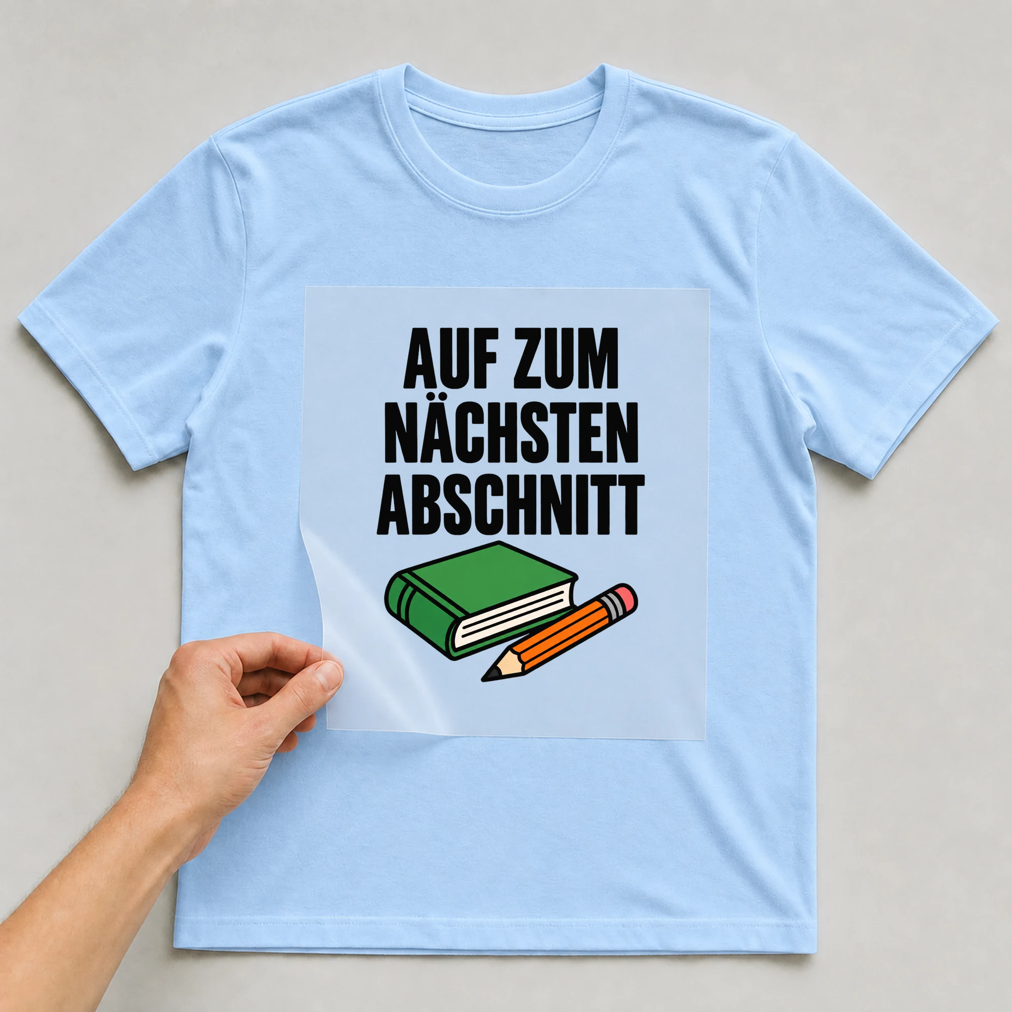 Bügelbild „Auf zum nächsten Abschnitt“ auf babyblauem T-Shirt, Folie wird aufgelegt