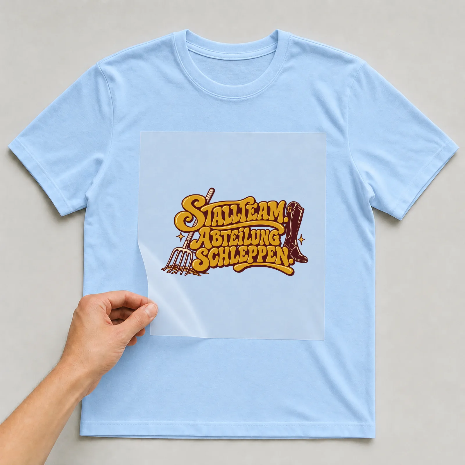 Bügelbild „Stallteam. Abteilung schleppen.“ auf hellblauem T-Shirt, Folie wird aufgelegt