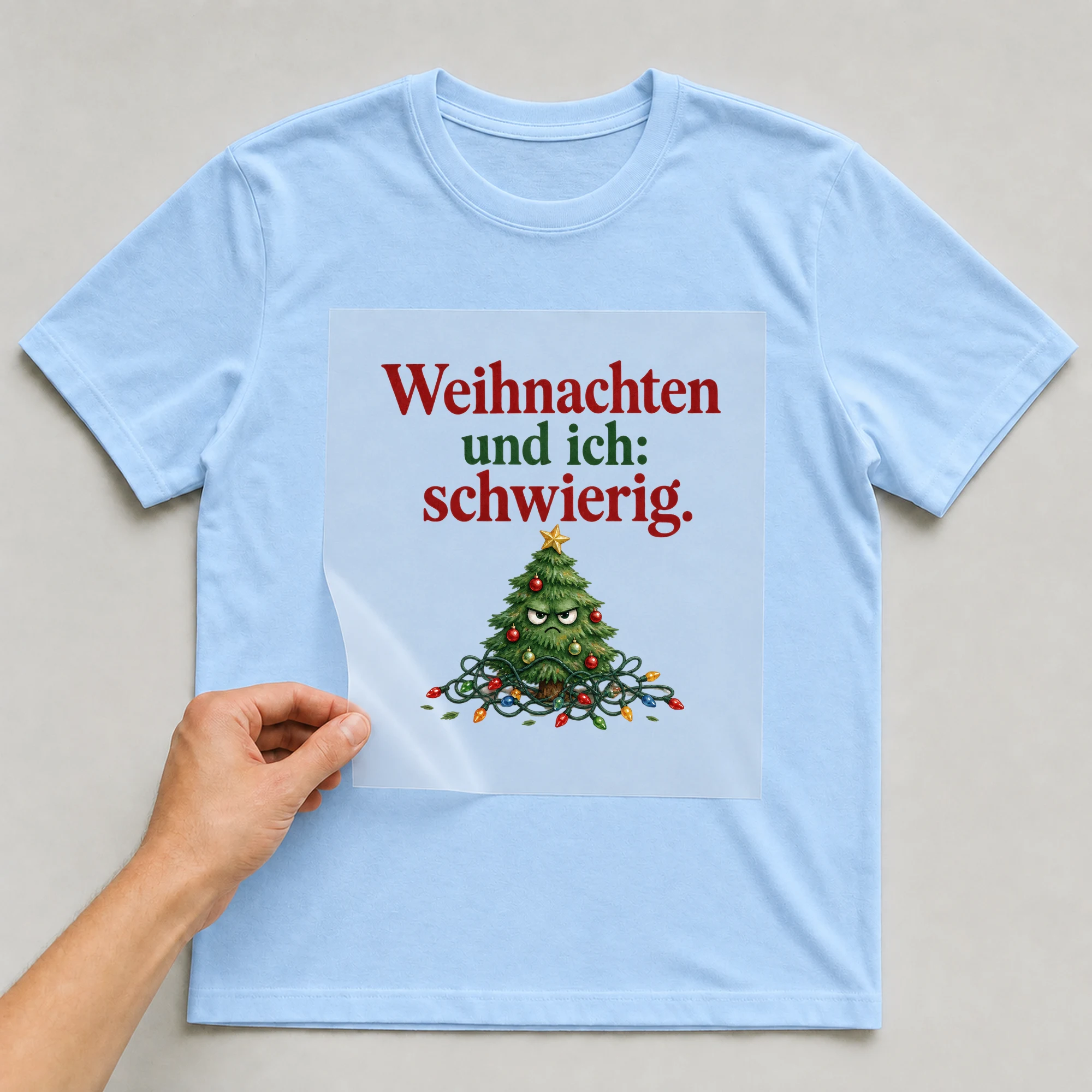 Bügelbild „Weihnachten und ich: schwierig.“ auf babyblauem T-Shirt, Folie wird aufgelegt