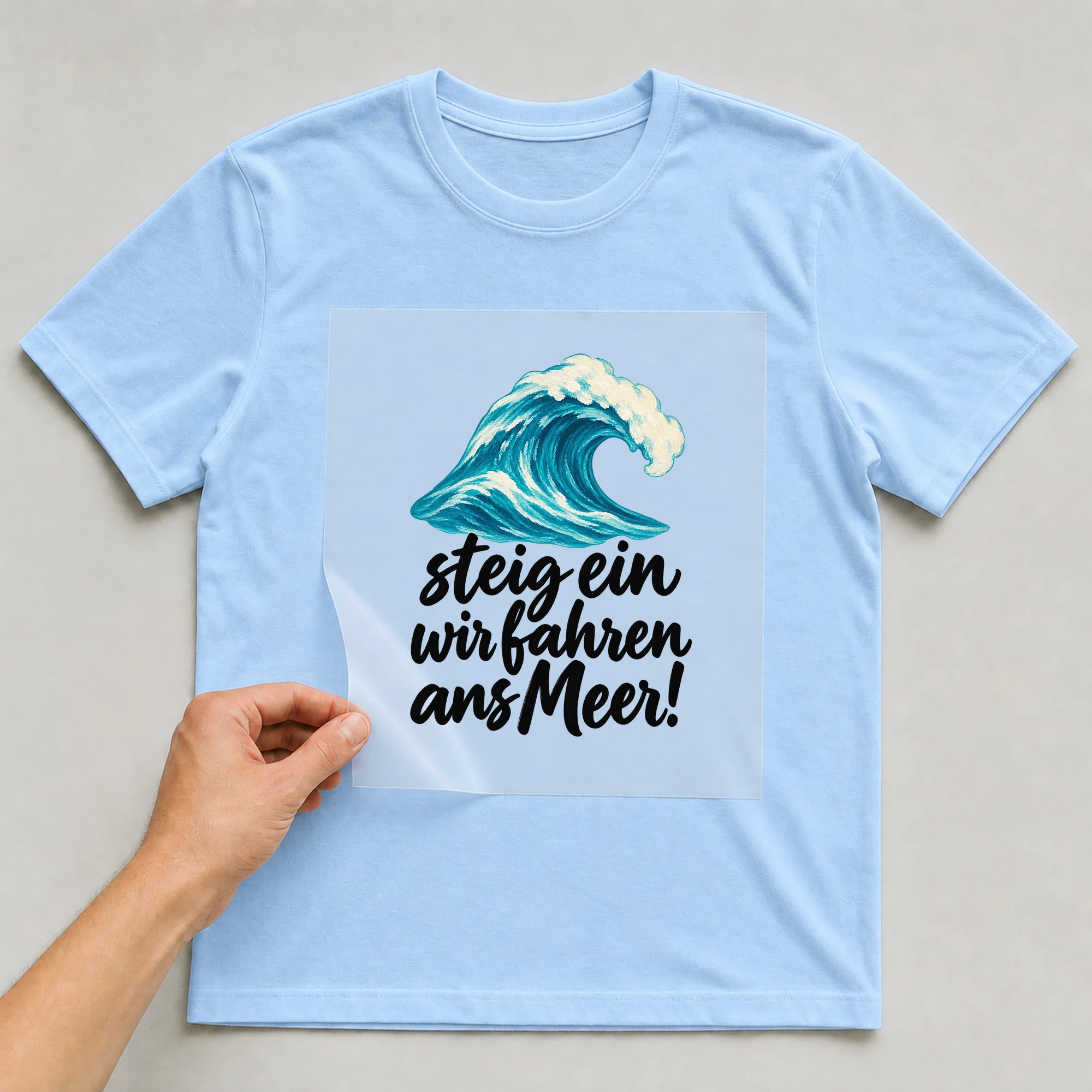 Bügelbild „steig ein wir fahren ans Meer!“ auf babyblauem T-Shirt, Folie wird aufgelegt