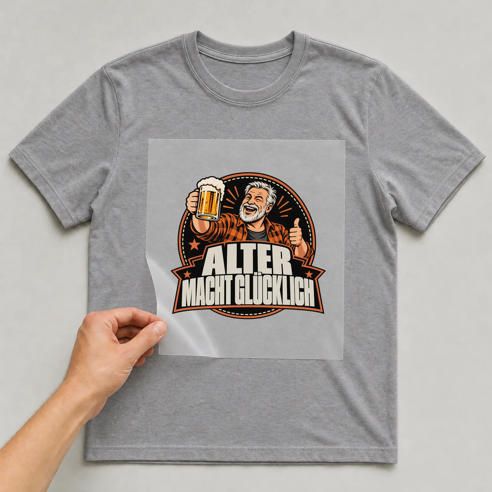 Bügelbild „Alter macht glücklich“ auf grauem T-Shirt, Folie wird aufgelegt