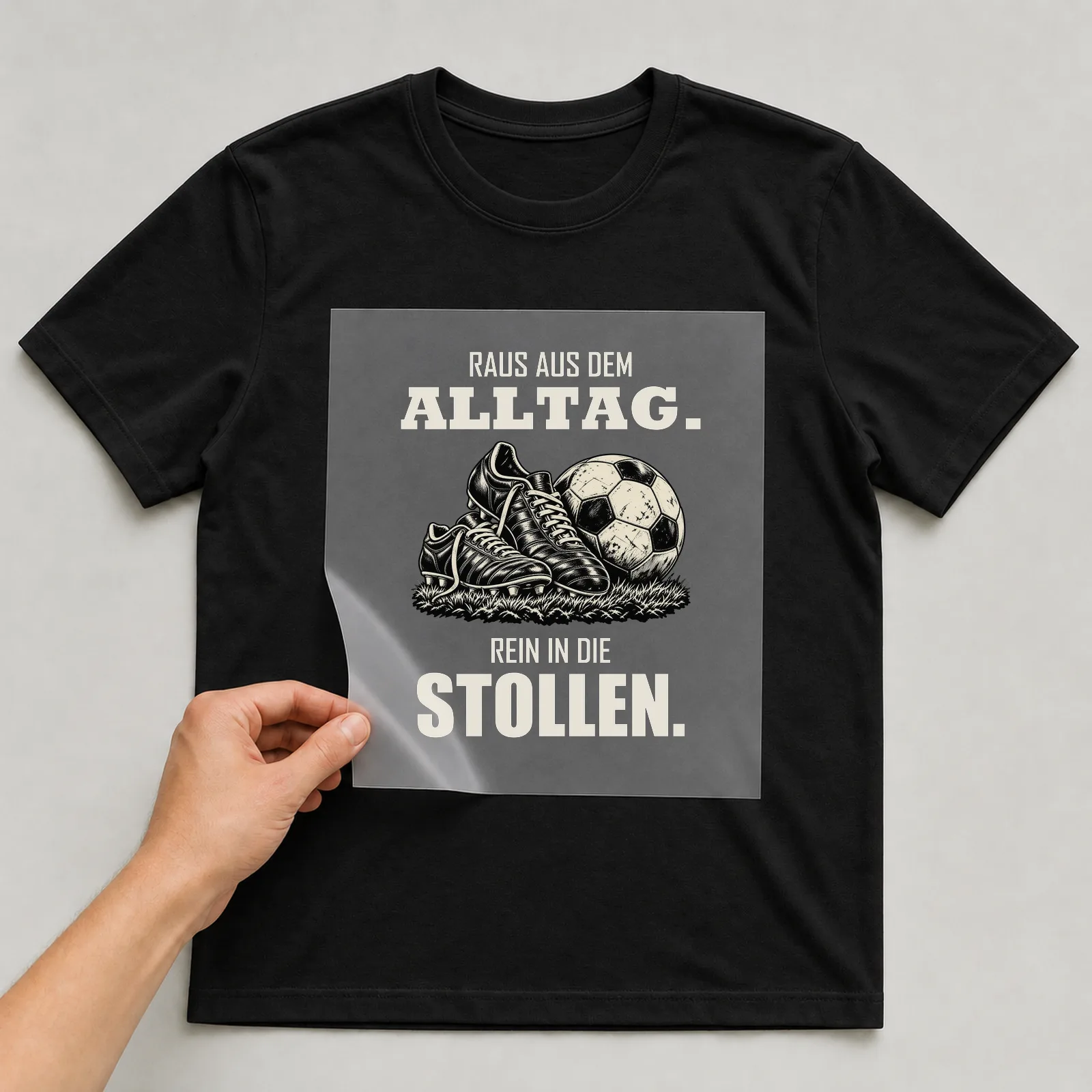 Bügelbild „Raus aus dem Alltag. Rein in die Stollen.“ auf schwarzem T-Shirt, Folie wird aufgelegt