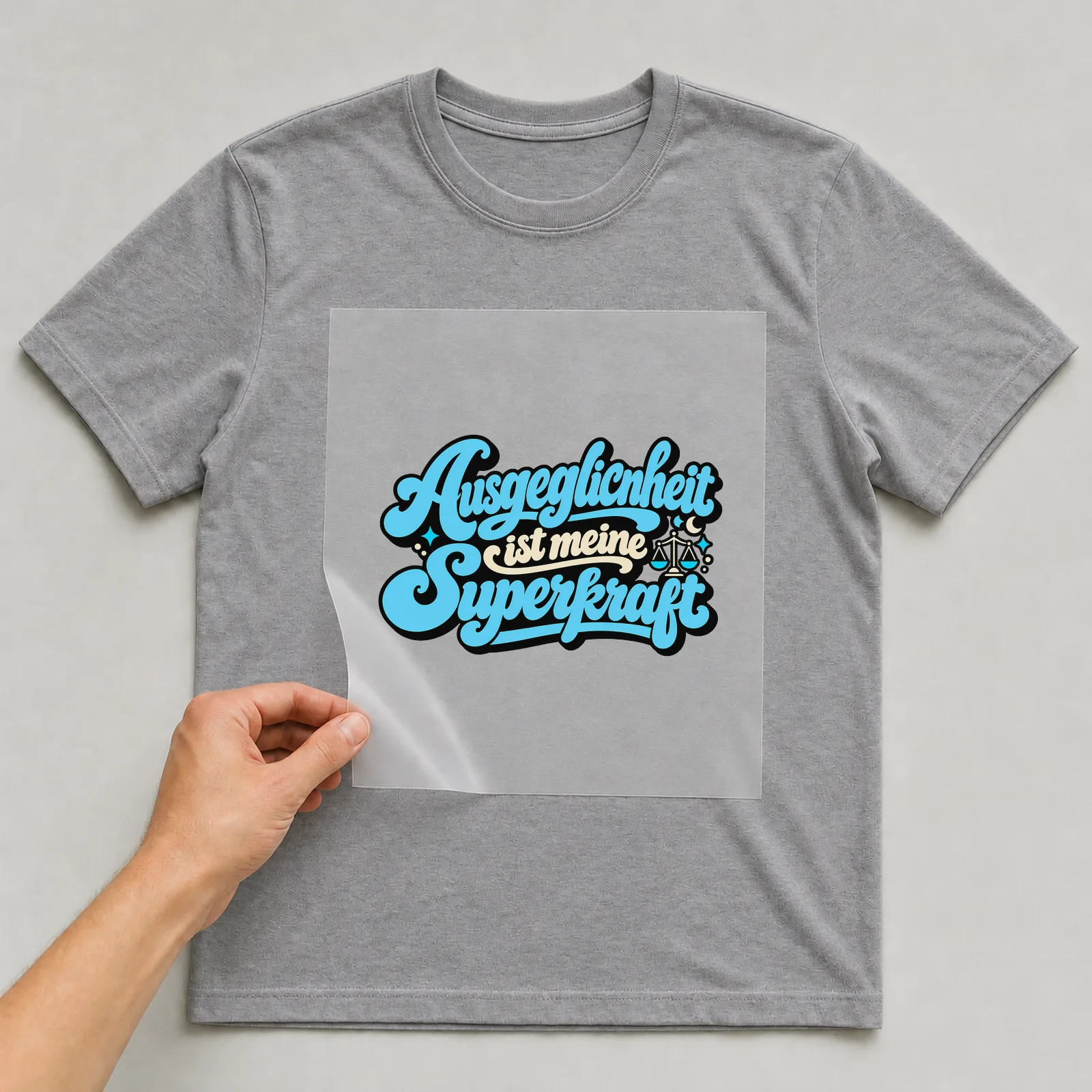 Bügelbild „Ausgeglichenheit ist meine Superkraft“ auf grauem T-Shirt, Folie wird aufgelegt