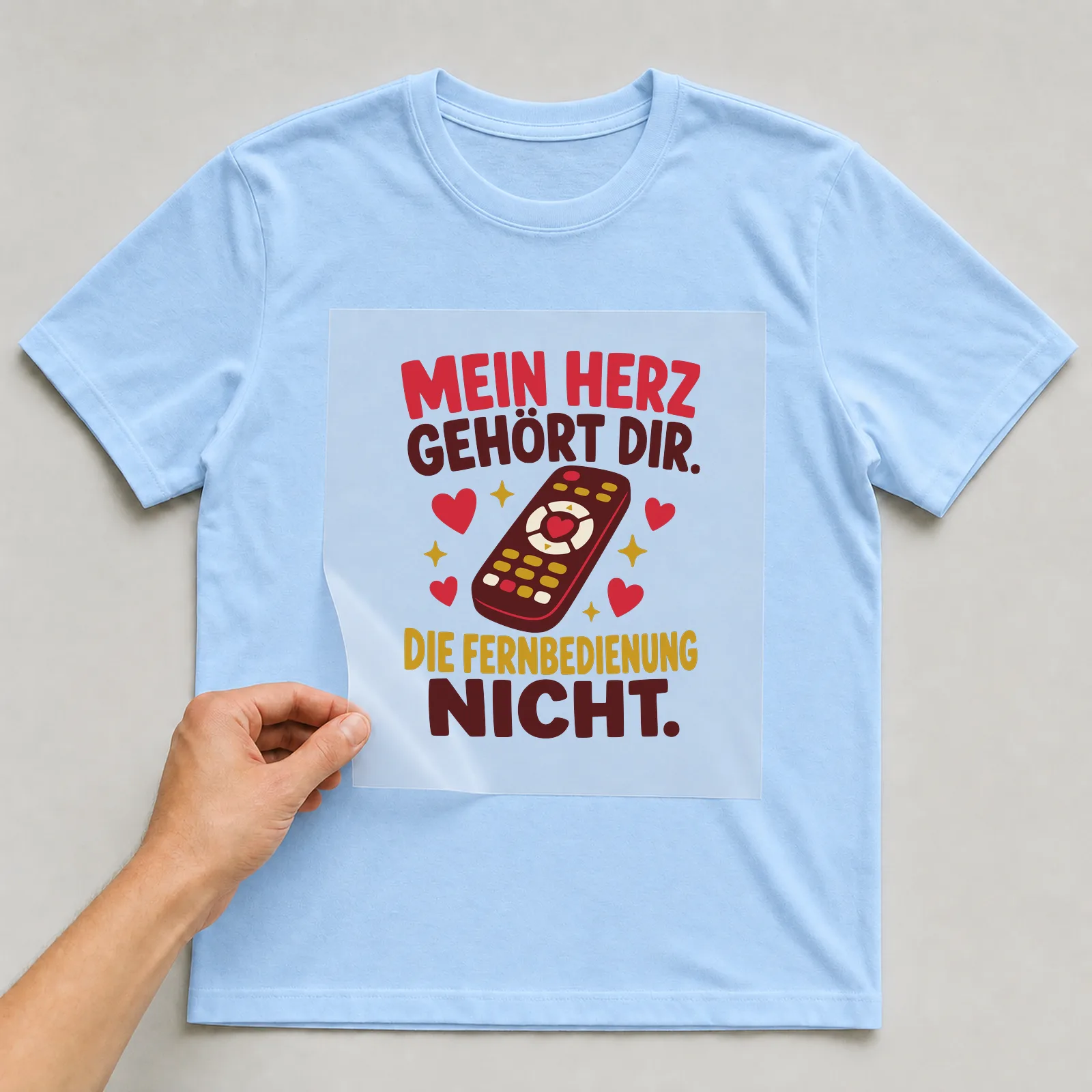 Bügelbild Mein Herz gehört dir. Die Fernbedienung nicht. auf hellblauem T-Shirt, Folie wird aufgelegt