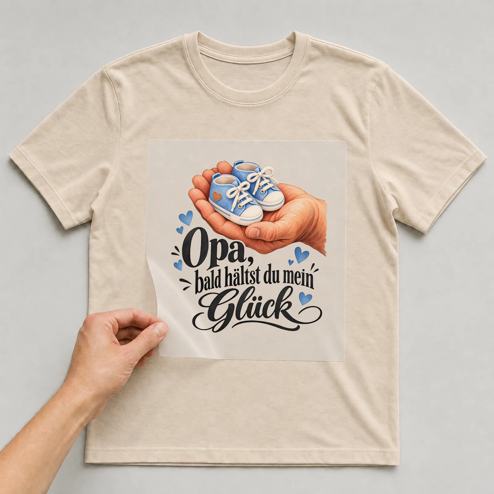 Bügelbild „Opa, bald hältst du mein Glück“ auf beigem T-Shirt, Folie wird aufgelegt