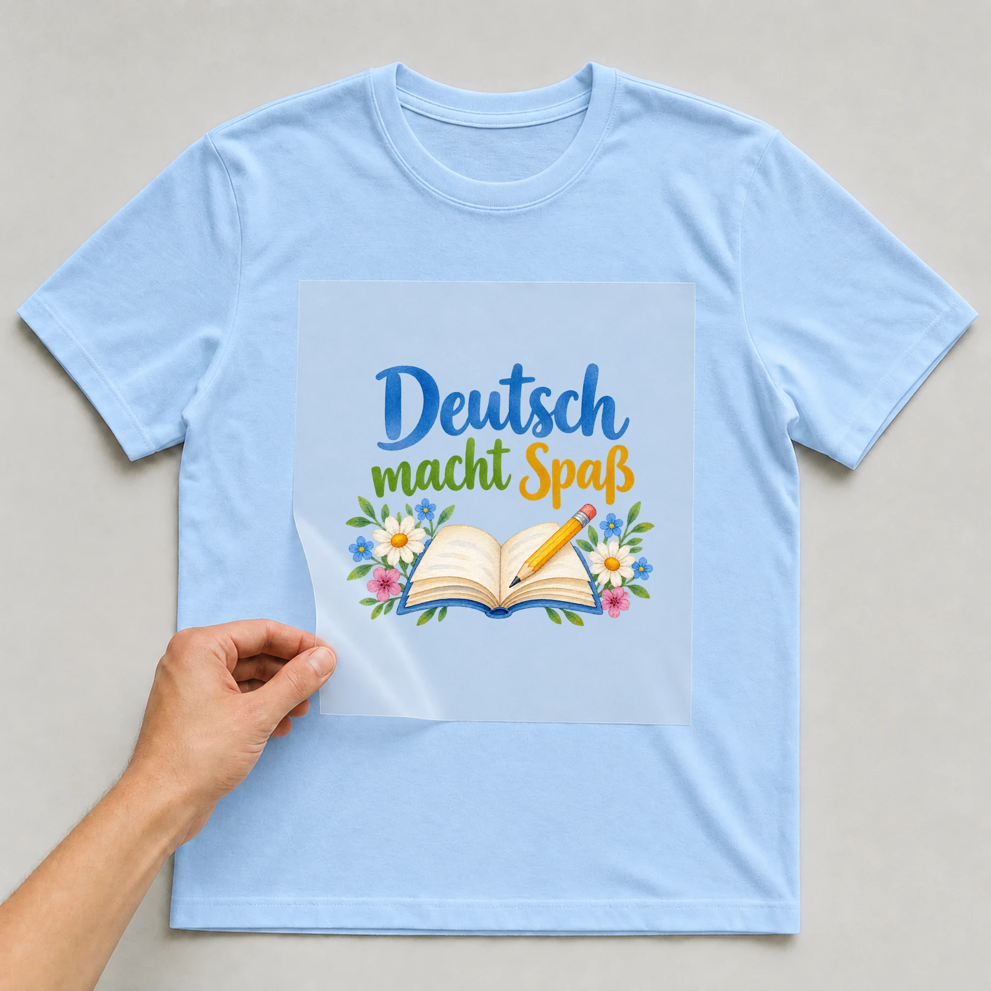 Bügelbild „Deutsch macht Spaß“ auf babyblauem T-Shirt, Folie wird aufgelegt