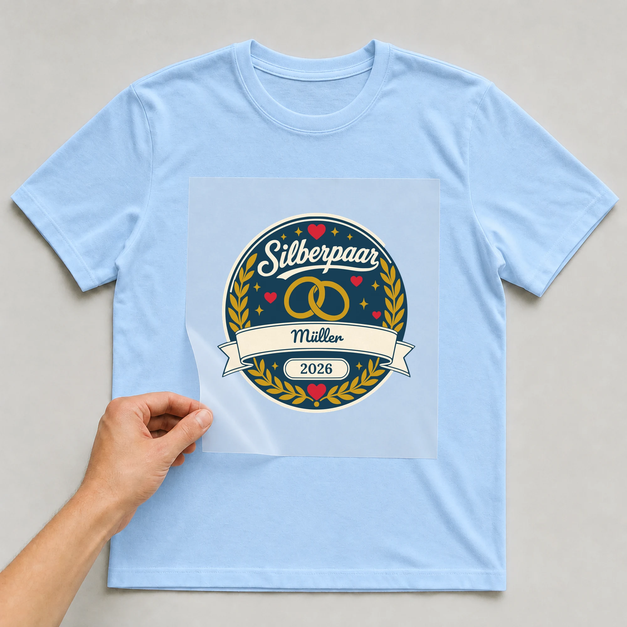 Bügelbild Silberpaar mit Nachname und Jahr auf hellblauem T-Shirt, Folie wird aufgelegt