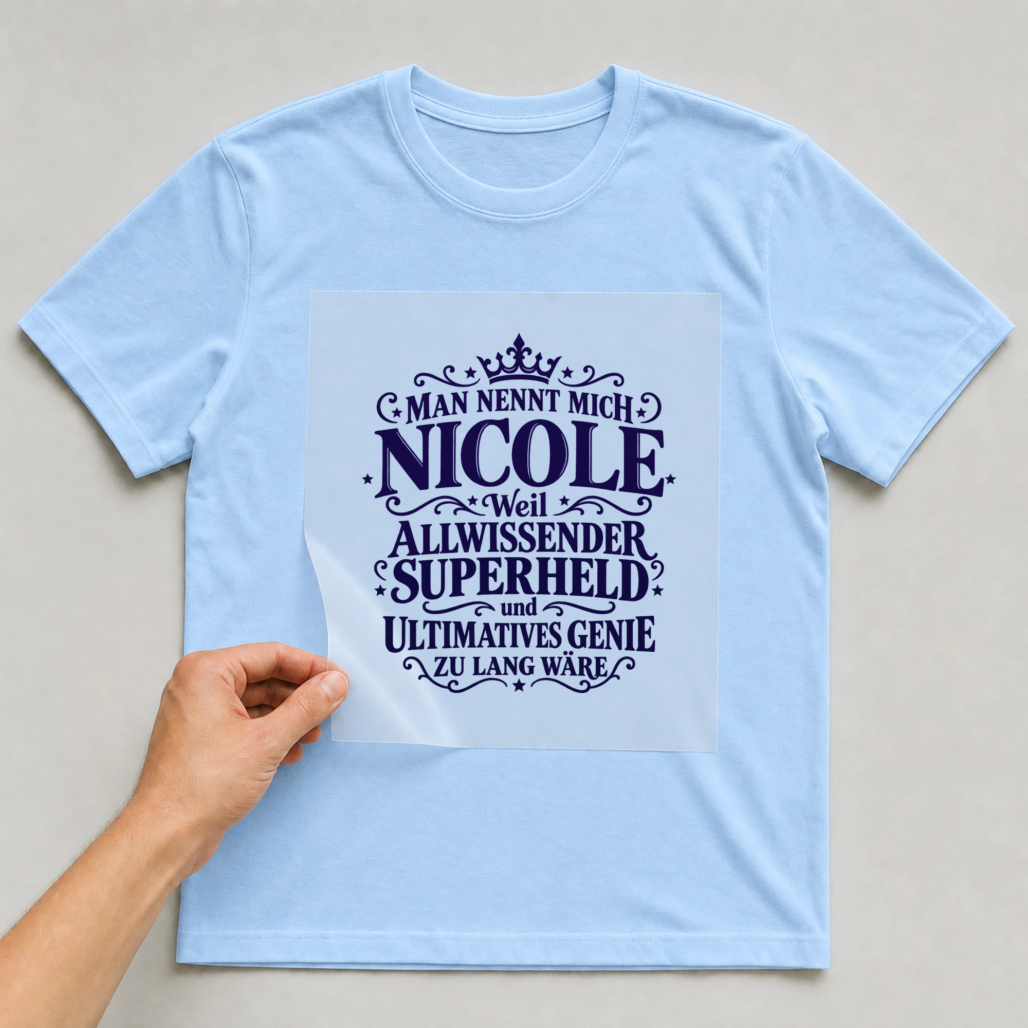 Bügelbild „Man nennt mich Nicole weil allwissender Superheld und ultimatives Genie zu“ auf babyblauem T-Shirt, Folie wird aufgelegt