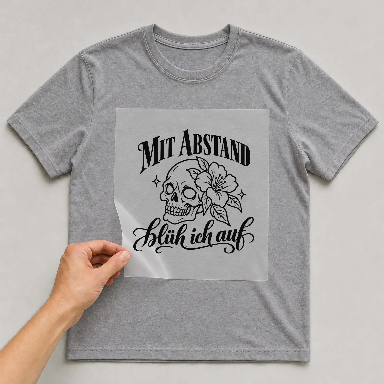 Bügelbild „Mit Abstand blüh ich auf“ auf grauem T-Shirt, Folie wird aufgelegt