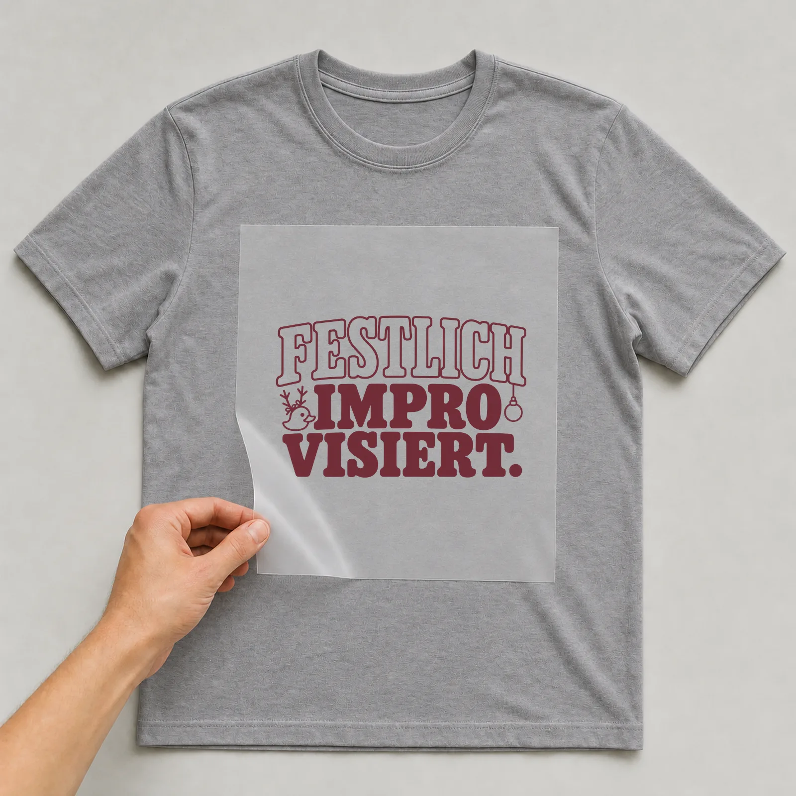 Bügelbild „Festlich improvisiert“ (Schrift Konturen, Nr. 2) auf grauem T-Shirt, Folie wird aufgelegt