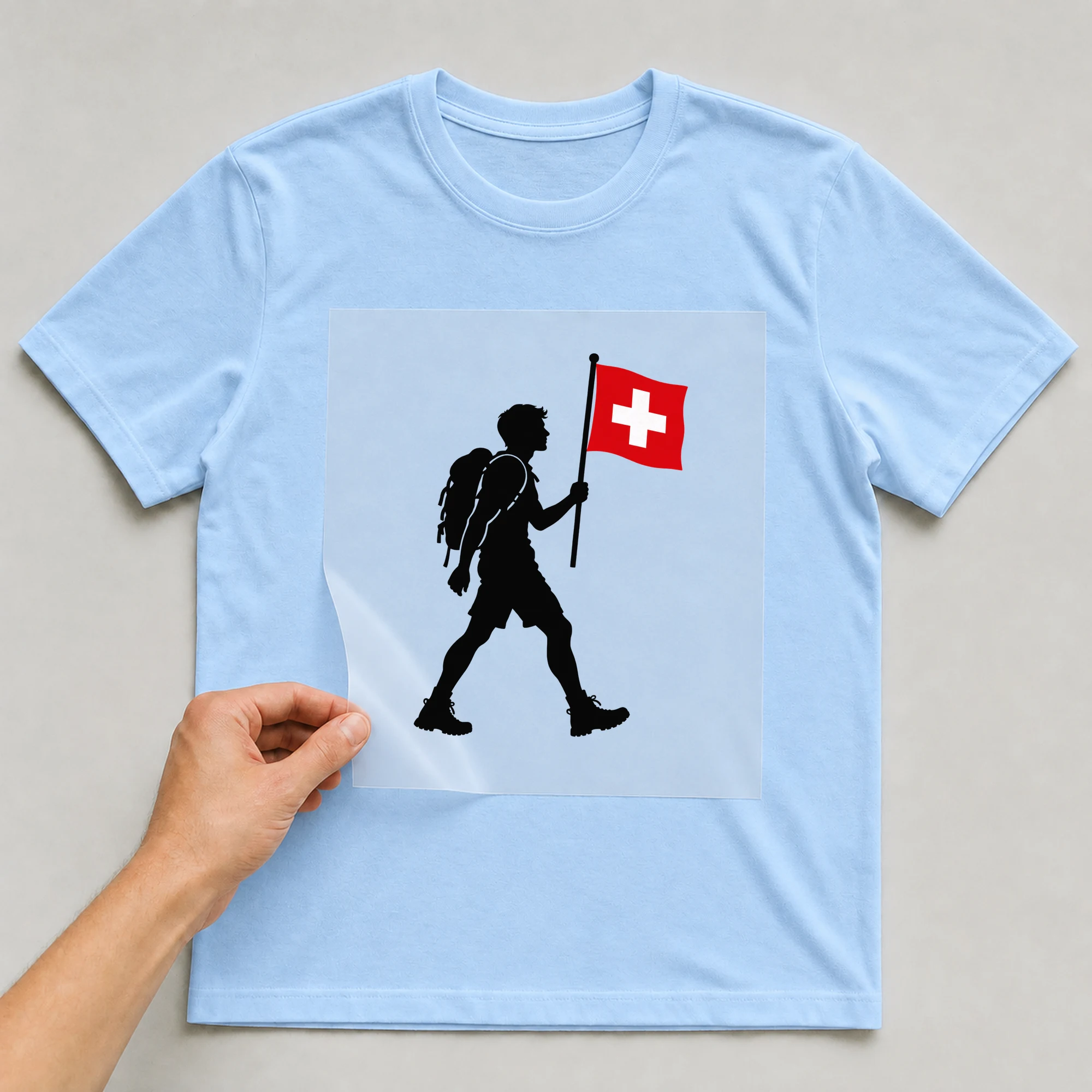 Bügelbild „Evolution Schweizer“ auf babyblauem T-Shirt, Folie wird aufgelegt