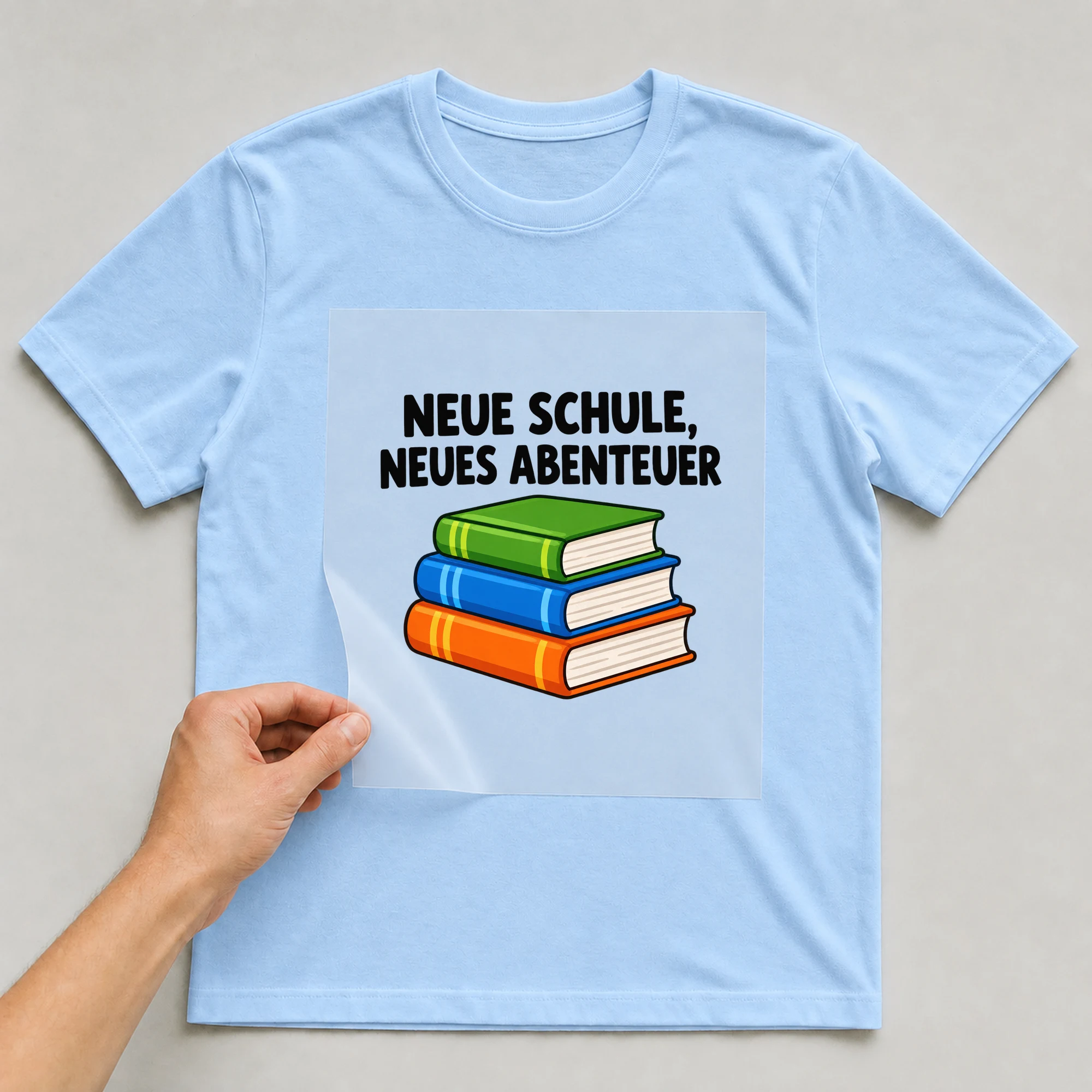 Bügelbild „Neue Schule, neues Abenteuer“ auf babyblauem T-Shirt, Folie wird aufgelegt