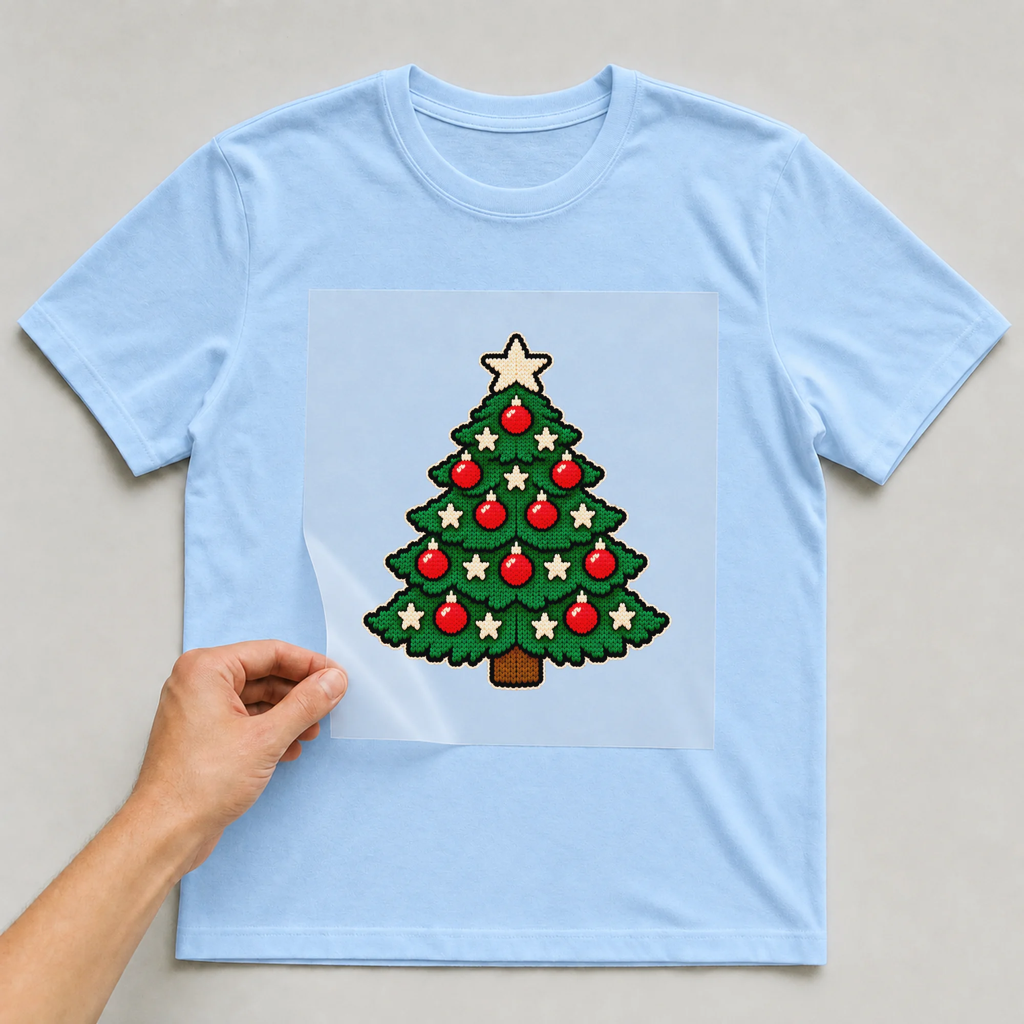 Bügelbild Gestrickter Weihnachtsbaum auf hellblauem T-Shirt, Folie wird aufgelegt