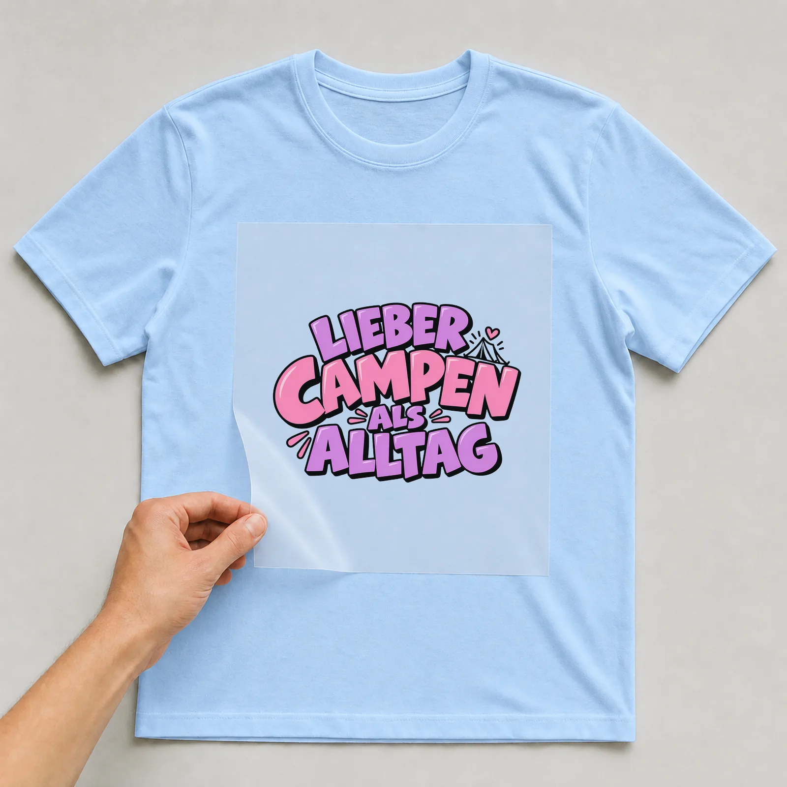 Bügelbild „Lieber campen als Alltag“ auf hellblauem T-Shirt, Folie wird aufgelegt