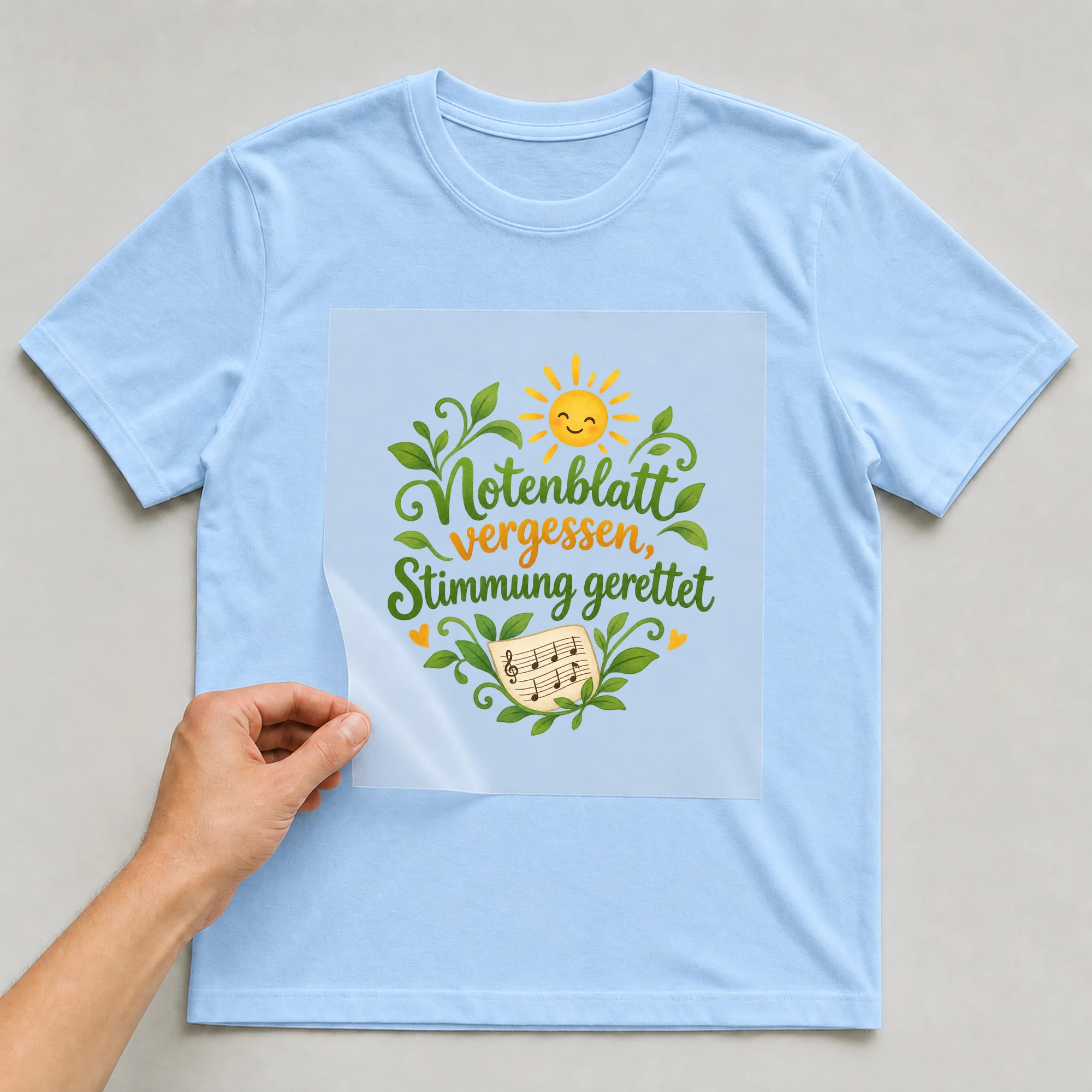 Bügelbild „Notenblatt vergessen, Stimmung gerettet“ auf babyblauem T-Shirt, Folie wird aufgelegt