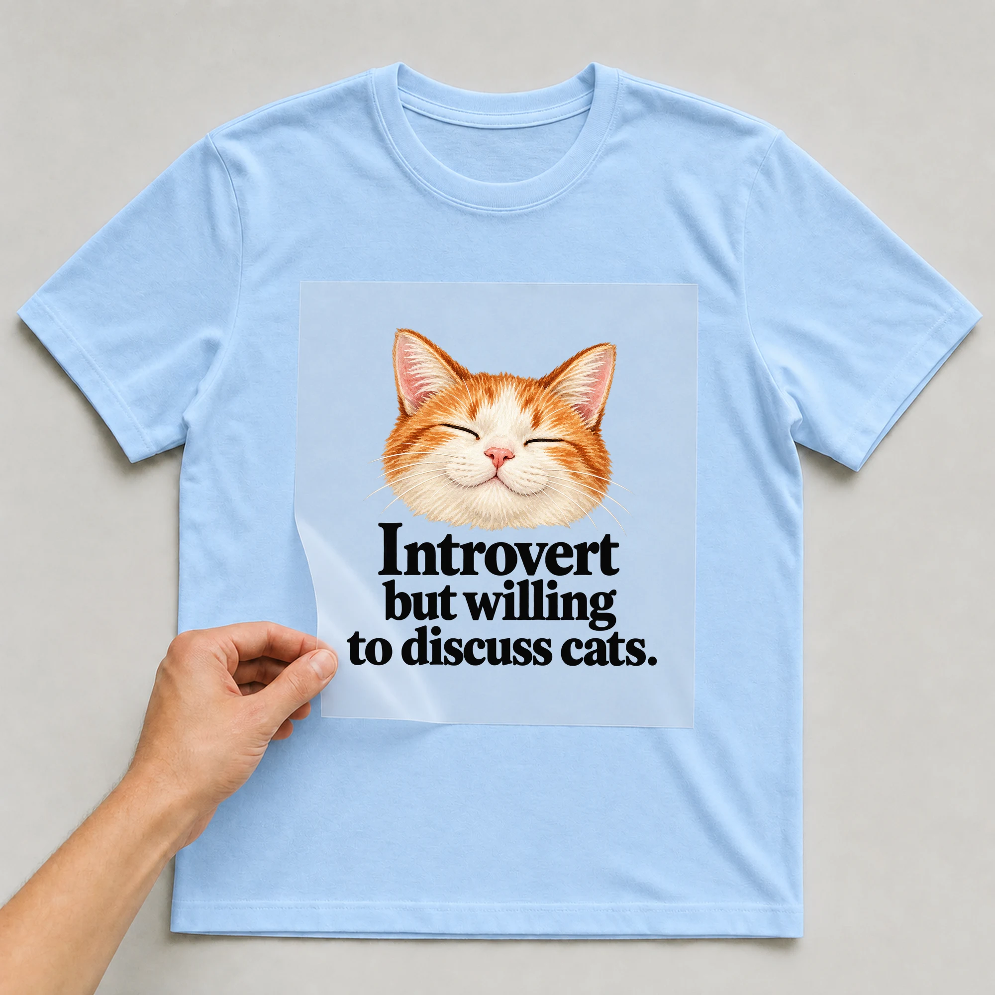 Bügelbild „Introvert but willing to discuss cats.“ auf babyblauem T-Shirt, Folie wird aufgelegt