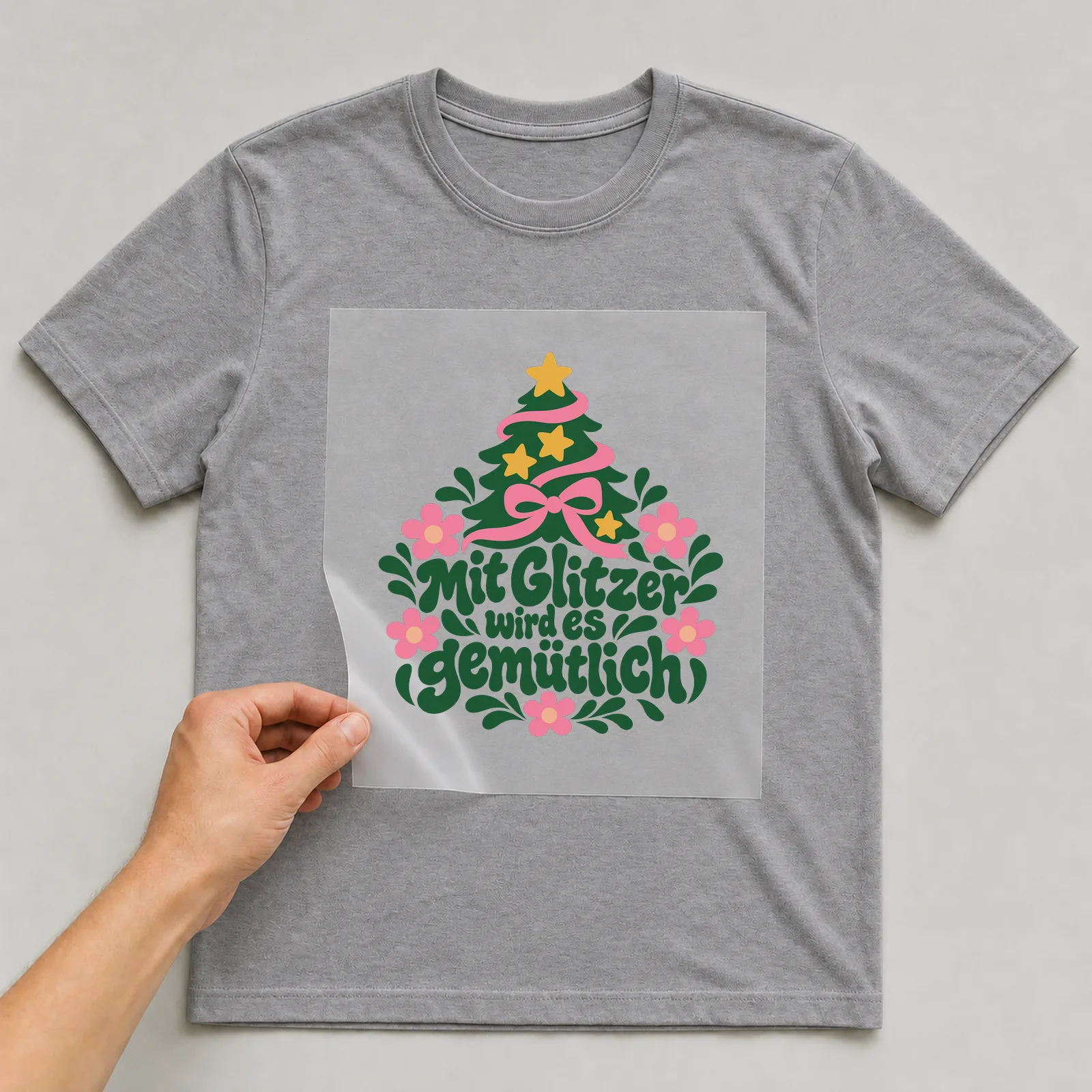 Bügelbild „Mit Glitzer wird es gemütlich“ auf grauem T-Shirt, Folie wird aufgelegt