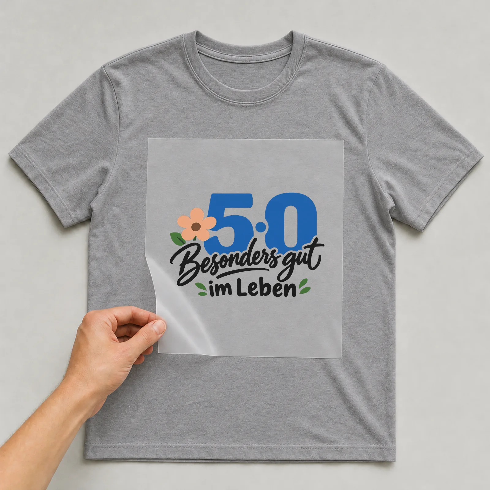 Bügelbild „50 · Besonders gut im Leben“ auf grauem T-Shirt, Folie wird aufgelegt
