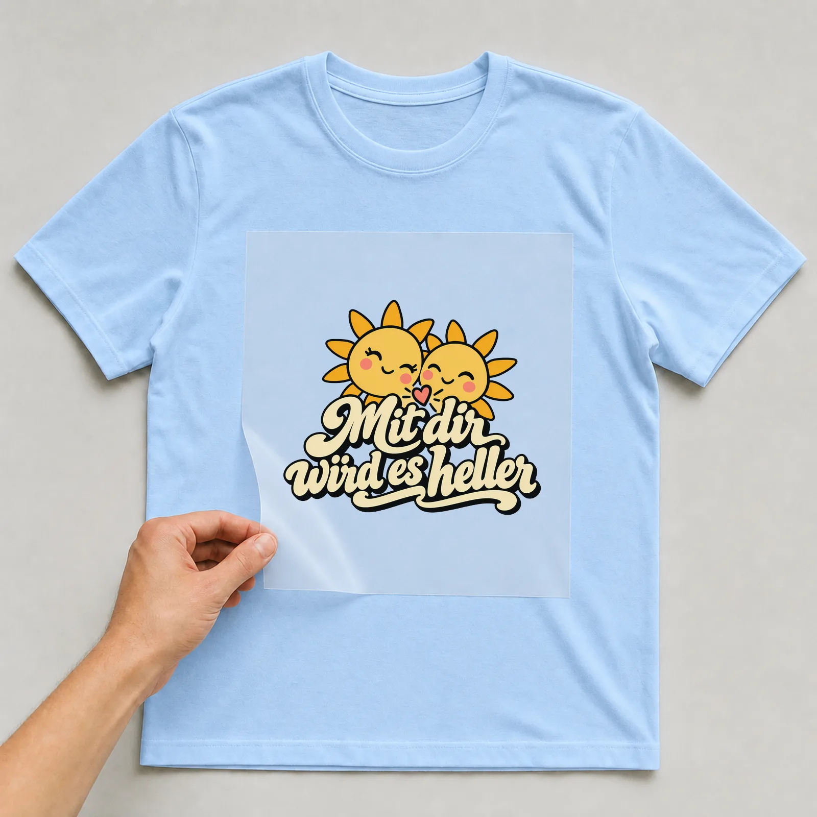 Bügelbild „Mit dir wird es heller“ auf hellblauem T-Shirt, Folie wird aufgelegt