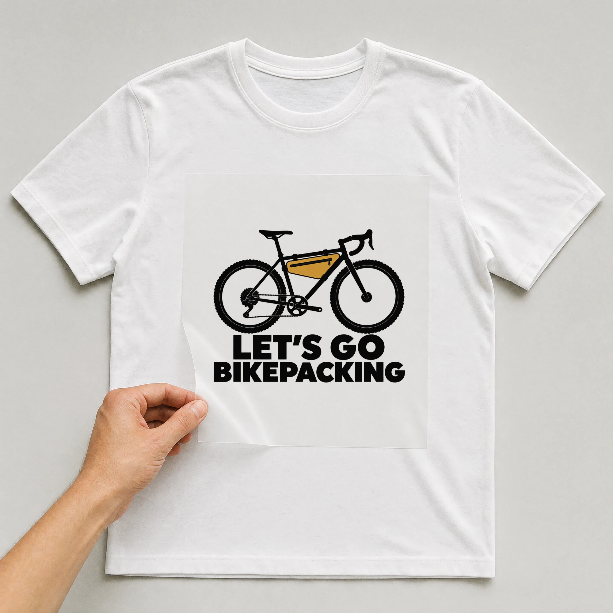 Bügelbild „Let's Go Bikepacking“ auf weißem T-Shirt, Folie wird aufgelegt
