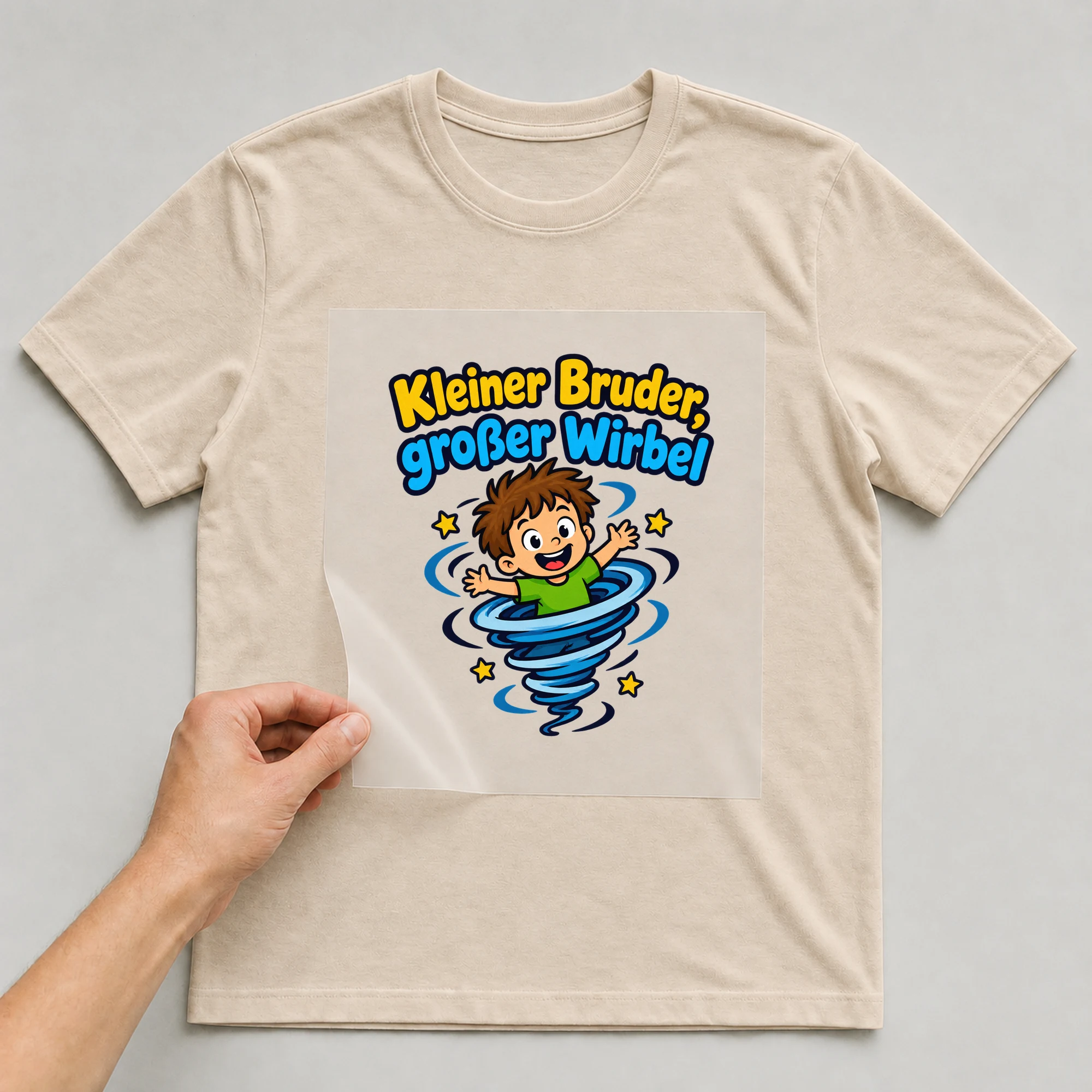 Bügelbild „Kleiner Bruder, großer Wirbel“ auf beigem T-Shirt, Folie wird aufgelegt