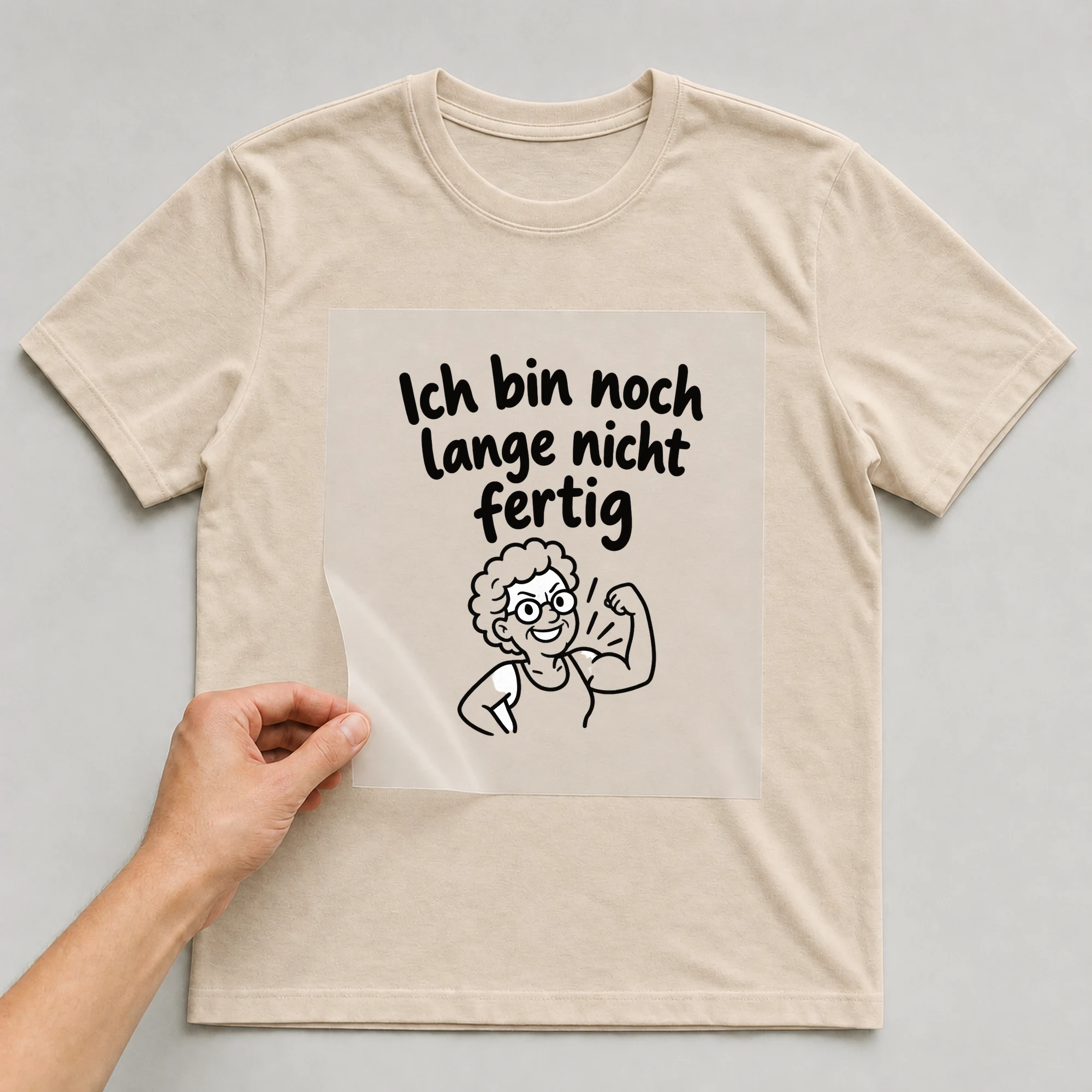 Bügelbild „Ich bin noch lange nicht fertig“ auf beigem T-Shirt, Folie wird aufgelegt