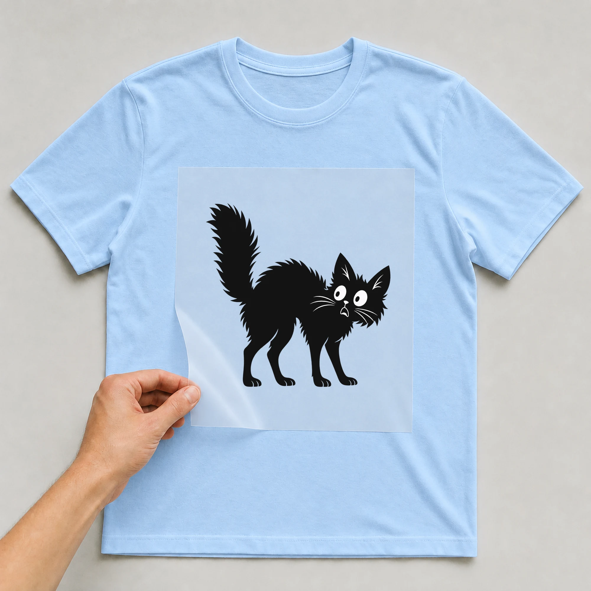 Bügelbild „Boo Cat“ auf babyblauem T-Shirt, Folie wird aufgelegt