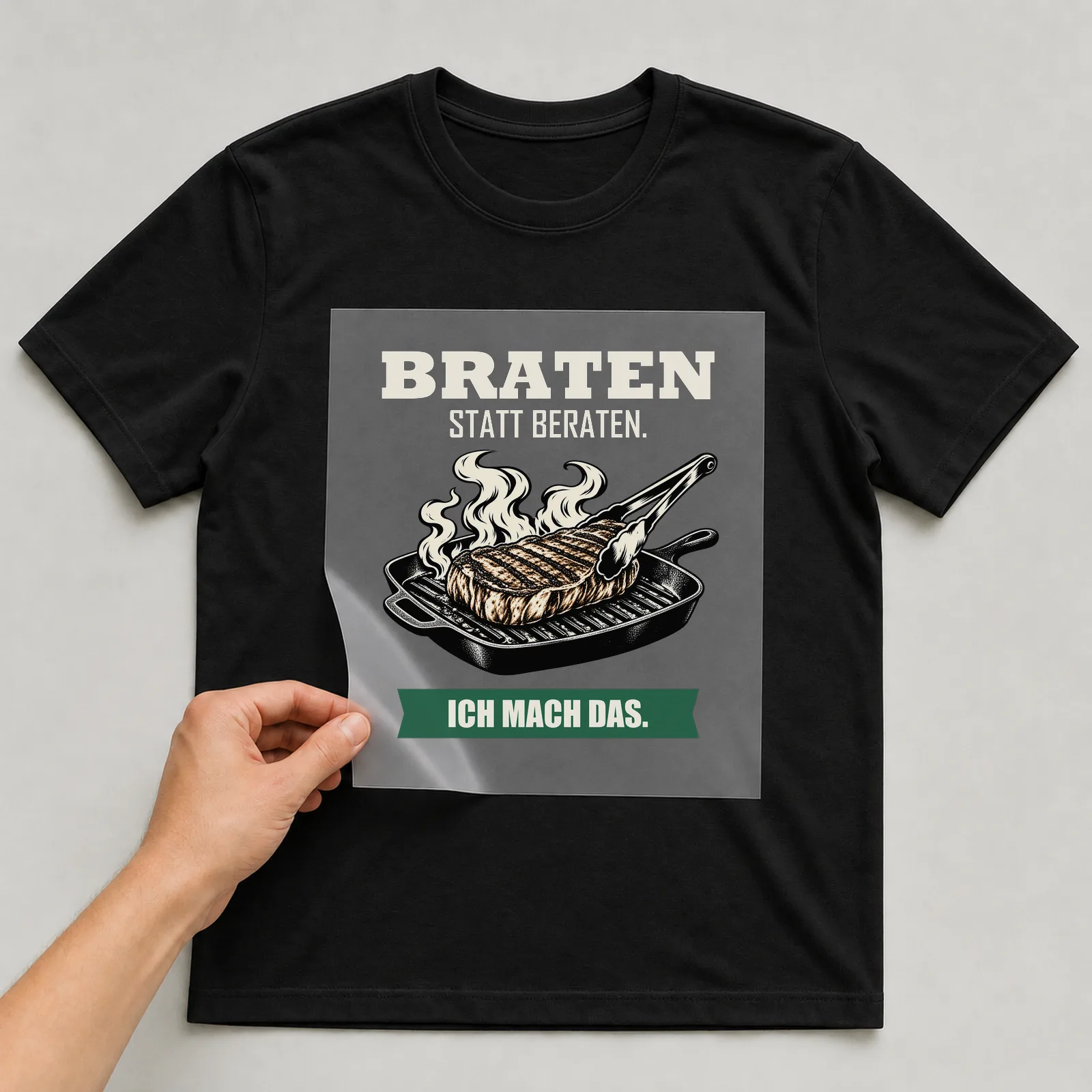 Bügelbild „Braten statt beraten. Ich mach das.“ auf schwarzem T-Shirt, Folie wird aufgelegt