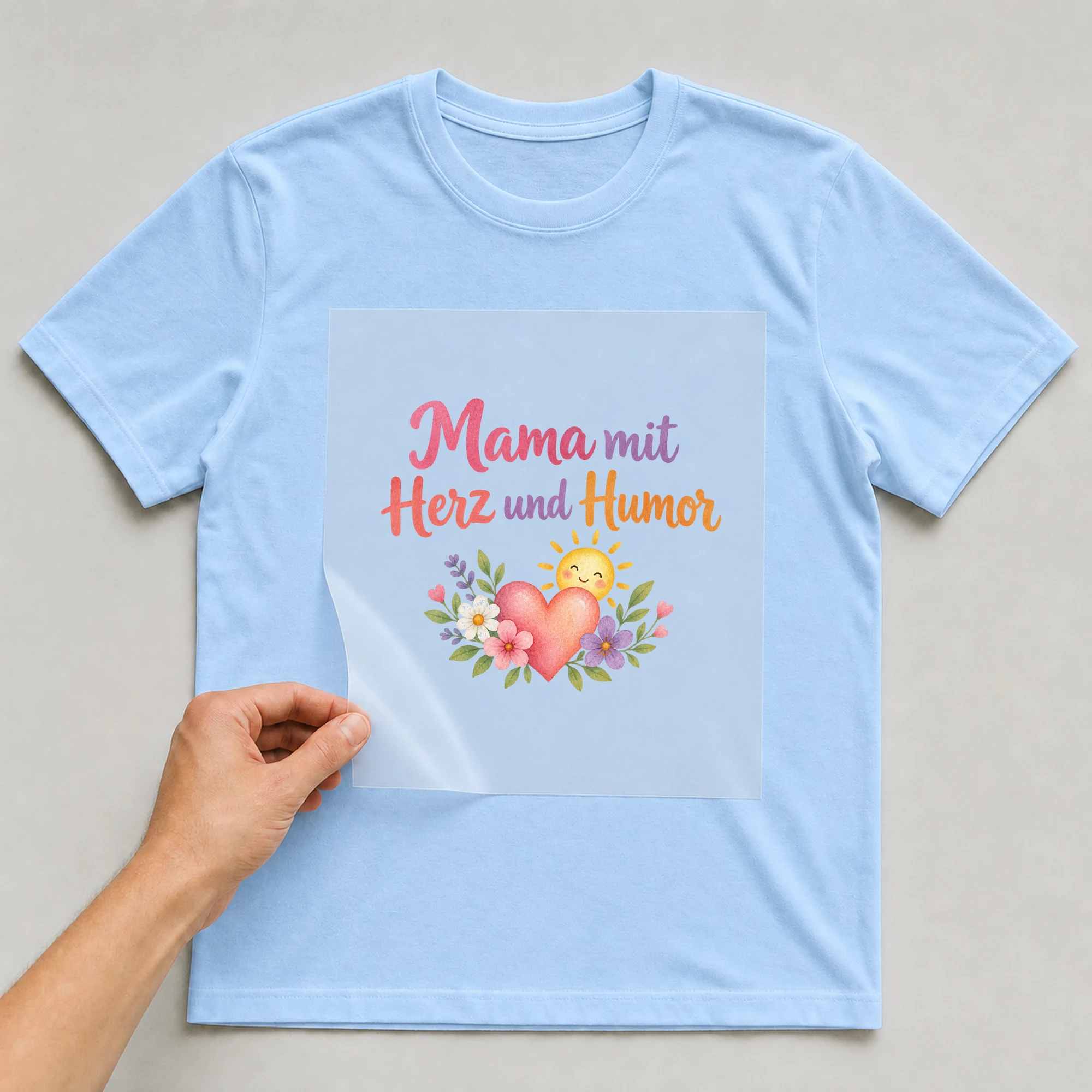 Bügelbild „Mama mit Herz und Humor“ auf babyblauem T-Shirt, Folie wird aufgelegt