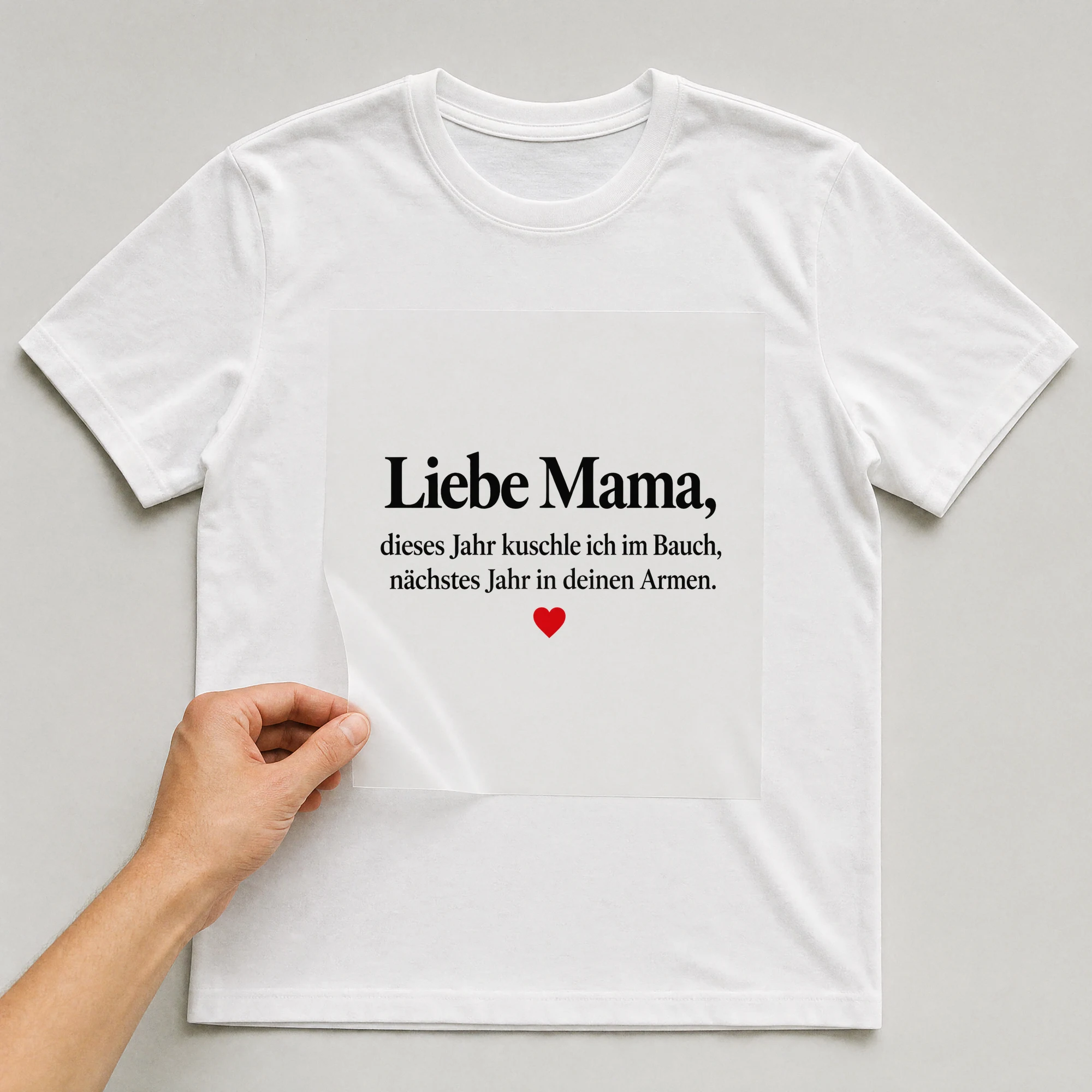 Bügelbild „Liebe Mama, dieses Jahr kuschle ich im Bauch, nächstes Jahr in deinen Armen.“ auf weißem T-Shirt, Folie wird aufgelegt