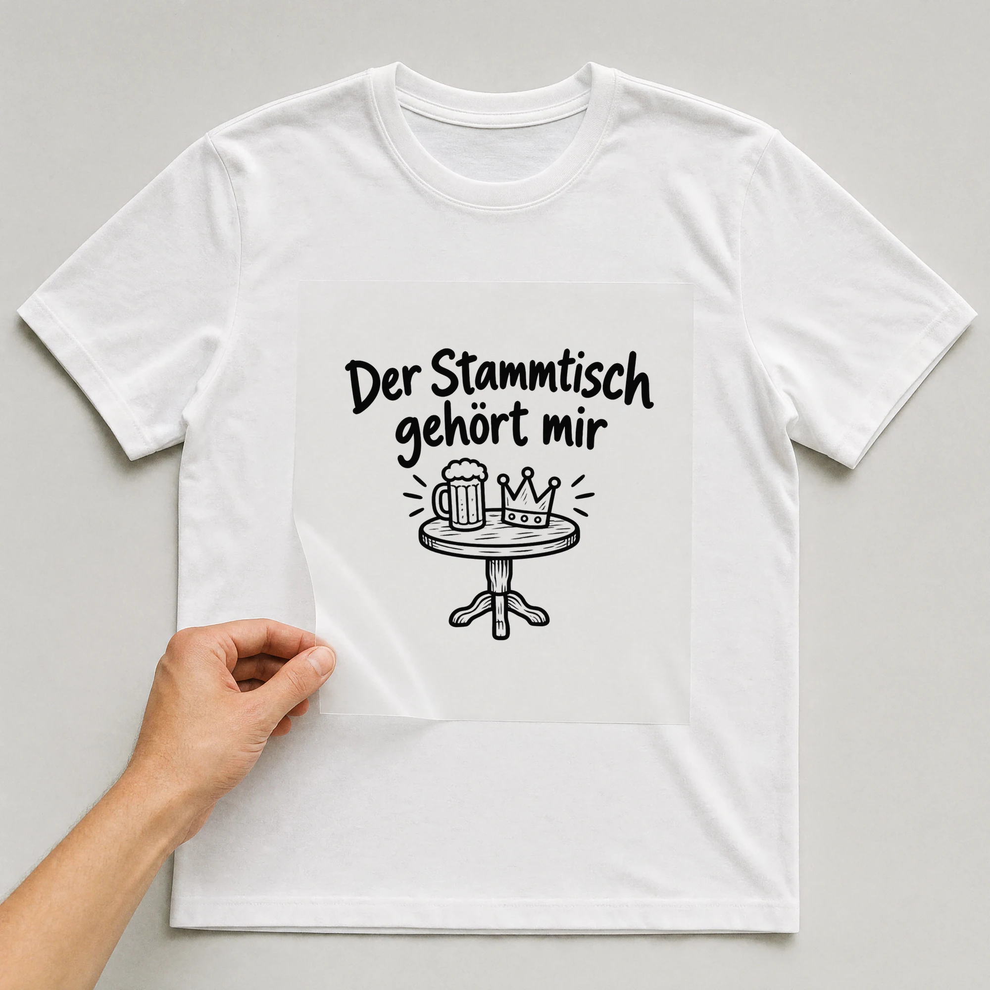 Bügelbild „Der Stammtisch gehört mir“ auf weißem T-Shirt, Folie wird aufgelegt