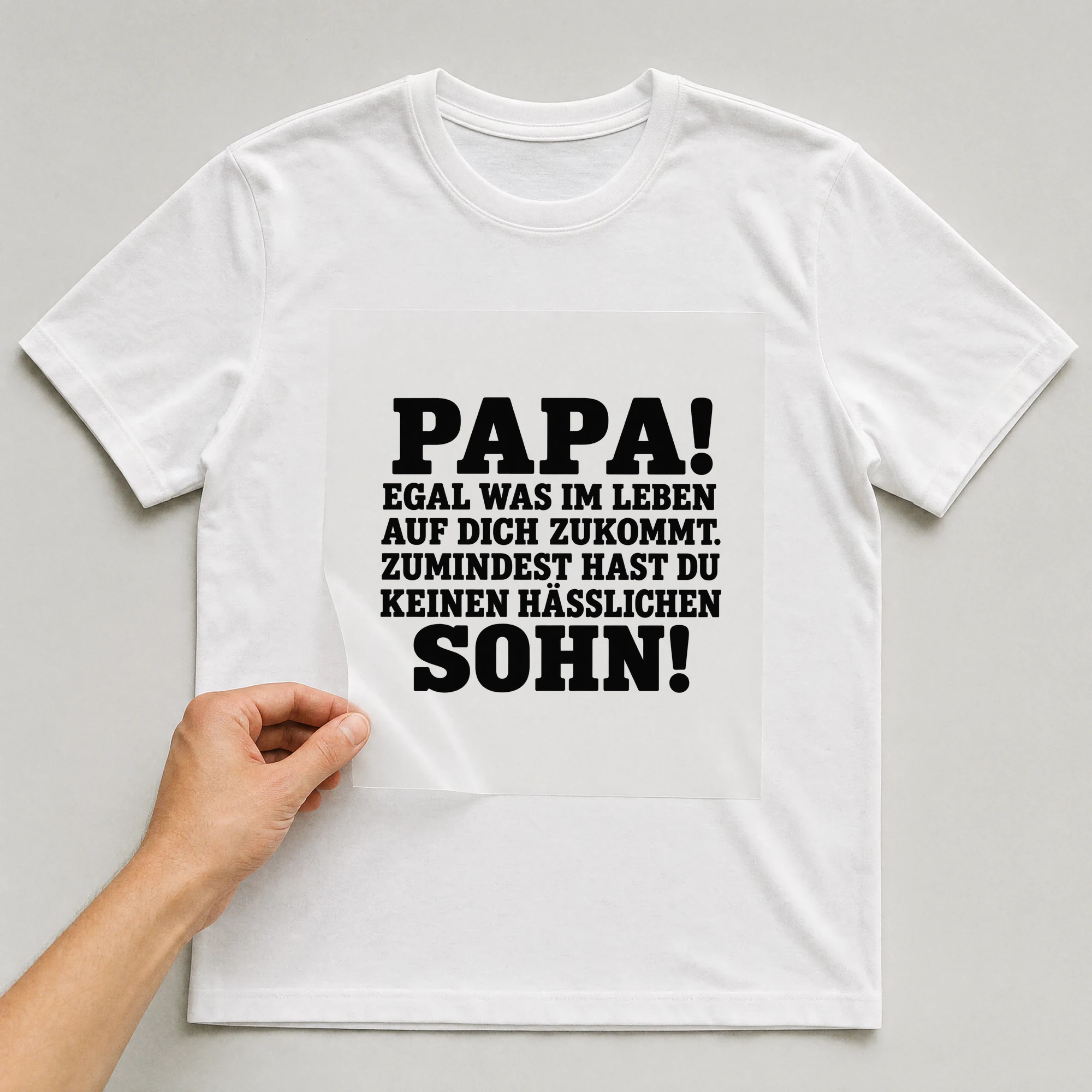 Bügelbild „Papa! Egal was im Leben auf dich zukommt. Zumindest hast du keinen Hässlichen“ auf weißem T-Shirt, Folie wird aufgelegt