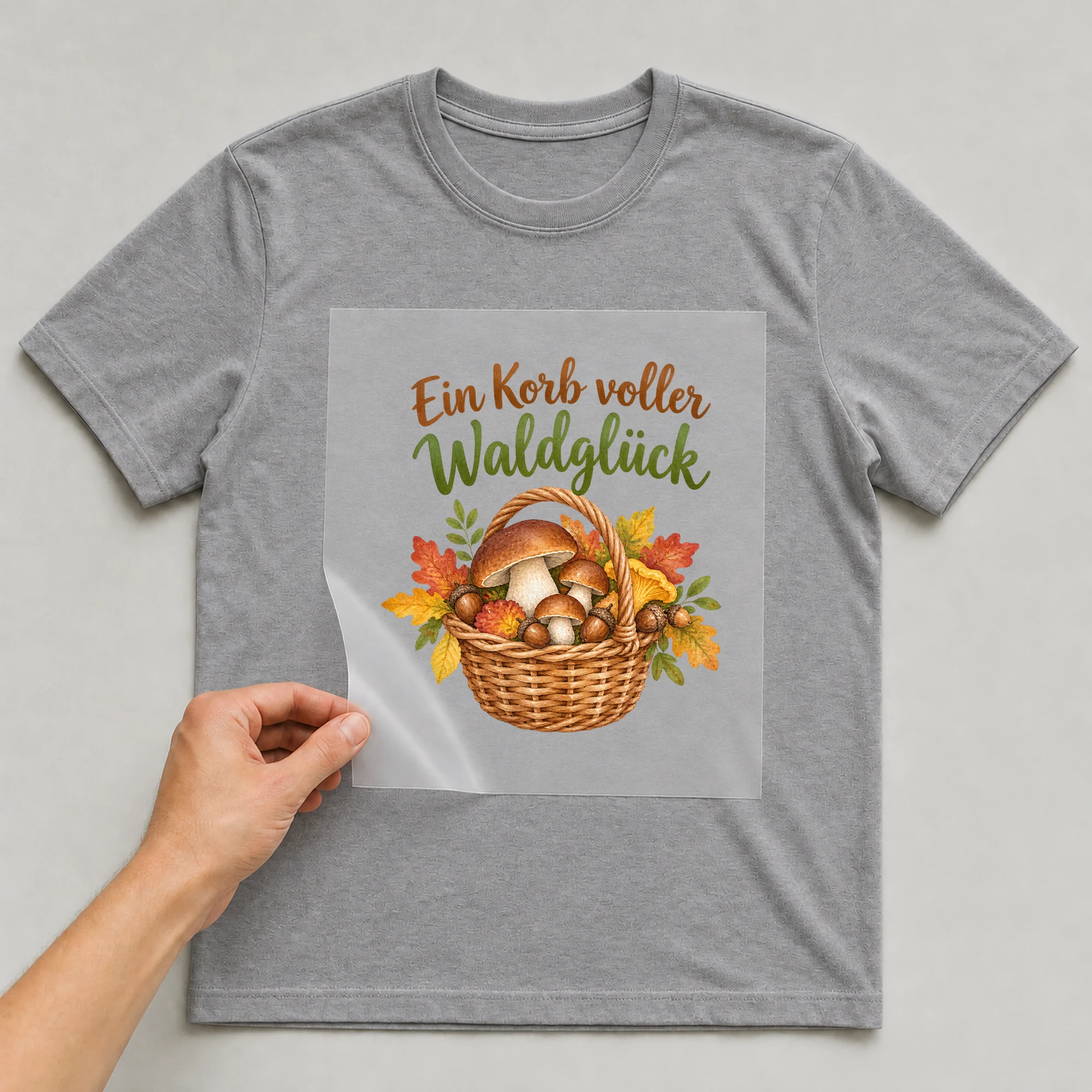 Bügelbild „Ein Korb voller Waldglück“ auf grauem T-Shirt, Folie wird aufgelegt