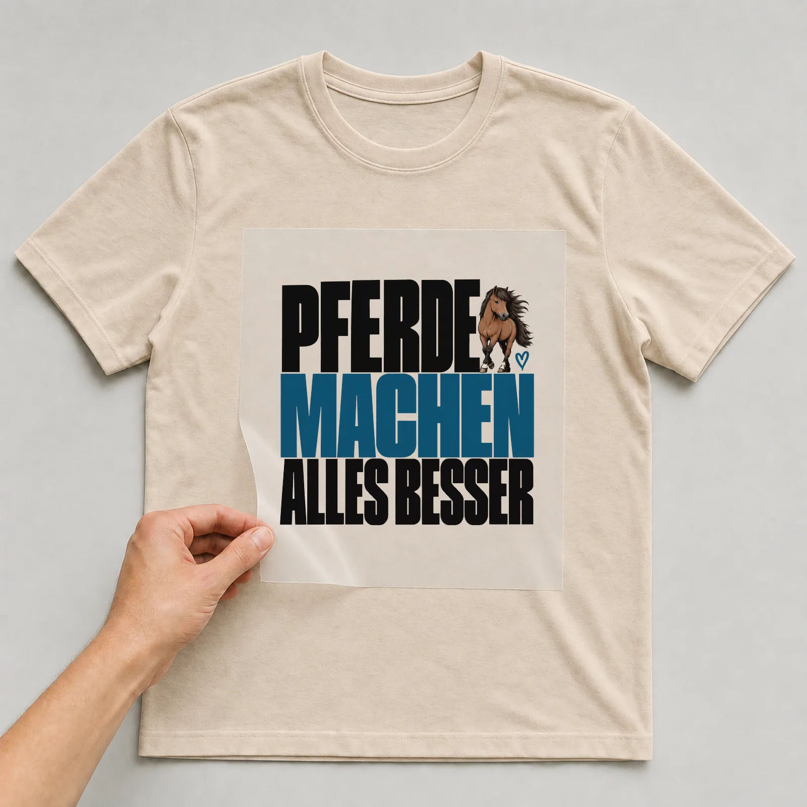 Bügelbild „Pferde machen alles besser“ (kompakter Plakatschrift) auf beigem T-Shirt, Folie wird aufgelegt