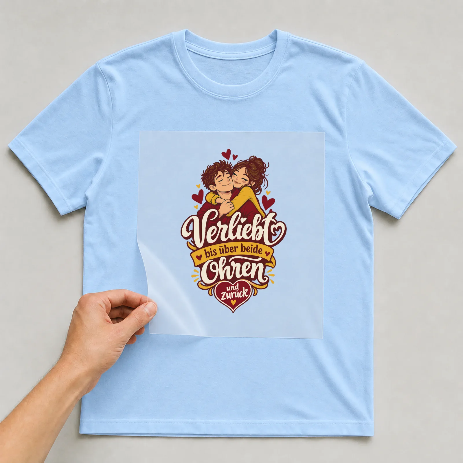 Bügelbild Verliebt bis über beide Ohren und zurück auf hellblauem T-Shirt, Folie wird aufgelegt