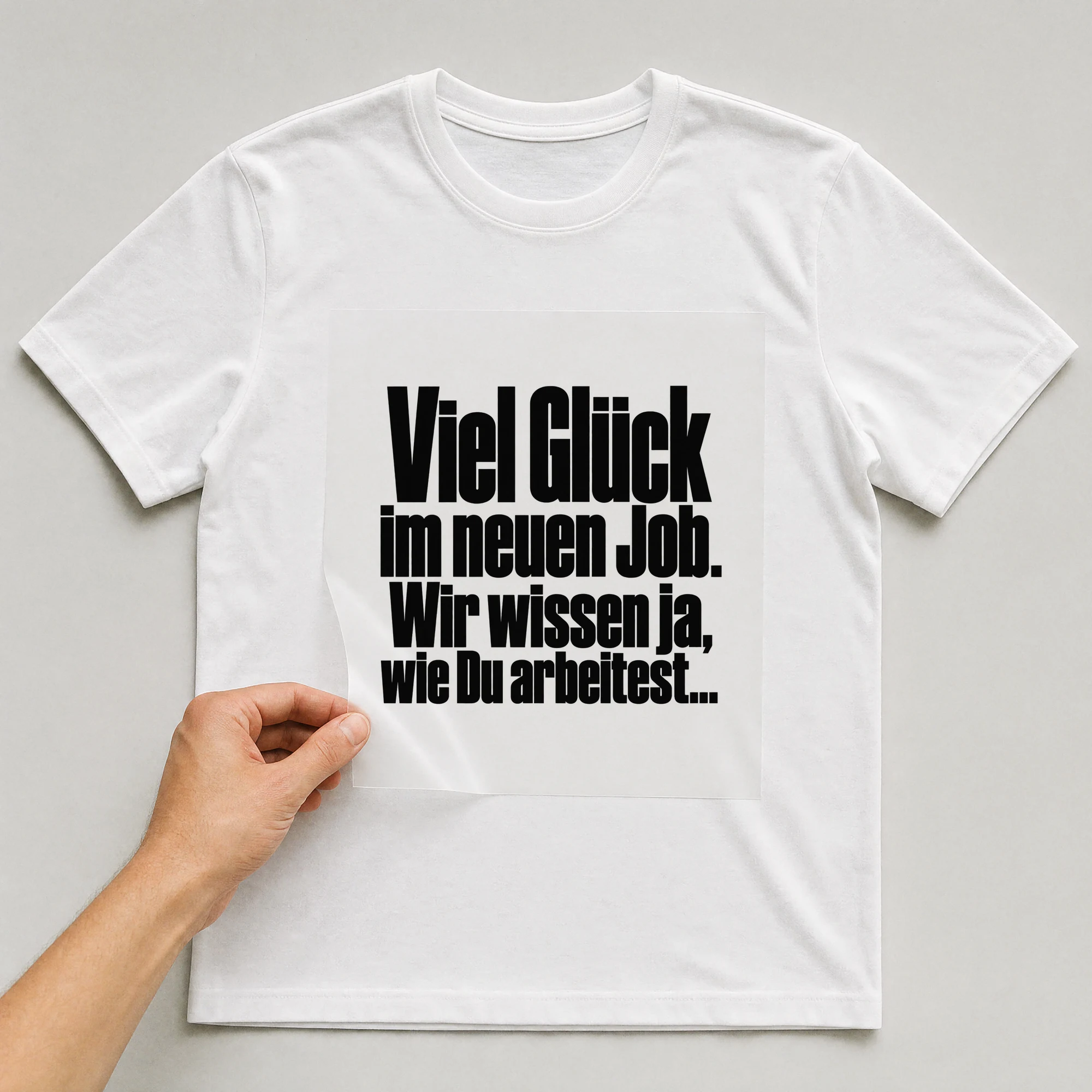 Bügelbild „Viel Glück im neuen Job. Wir wissen ja, wie Du arbeitest...“ auf weißem T-Shirt, Folie wird aufgelegt