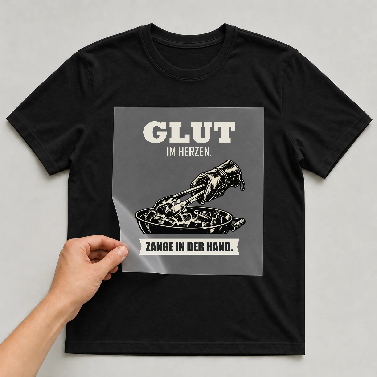 Bügelbild „Glut im herzen. Zange in der Hand.“ auf schwarzem T-Shirt, Folie wird aufgelegt