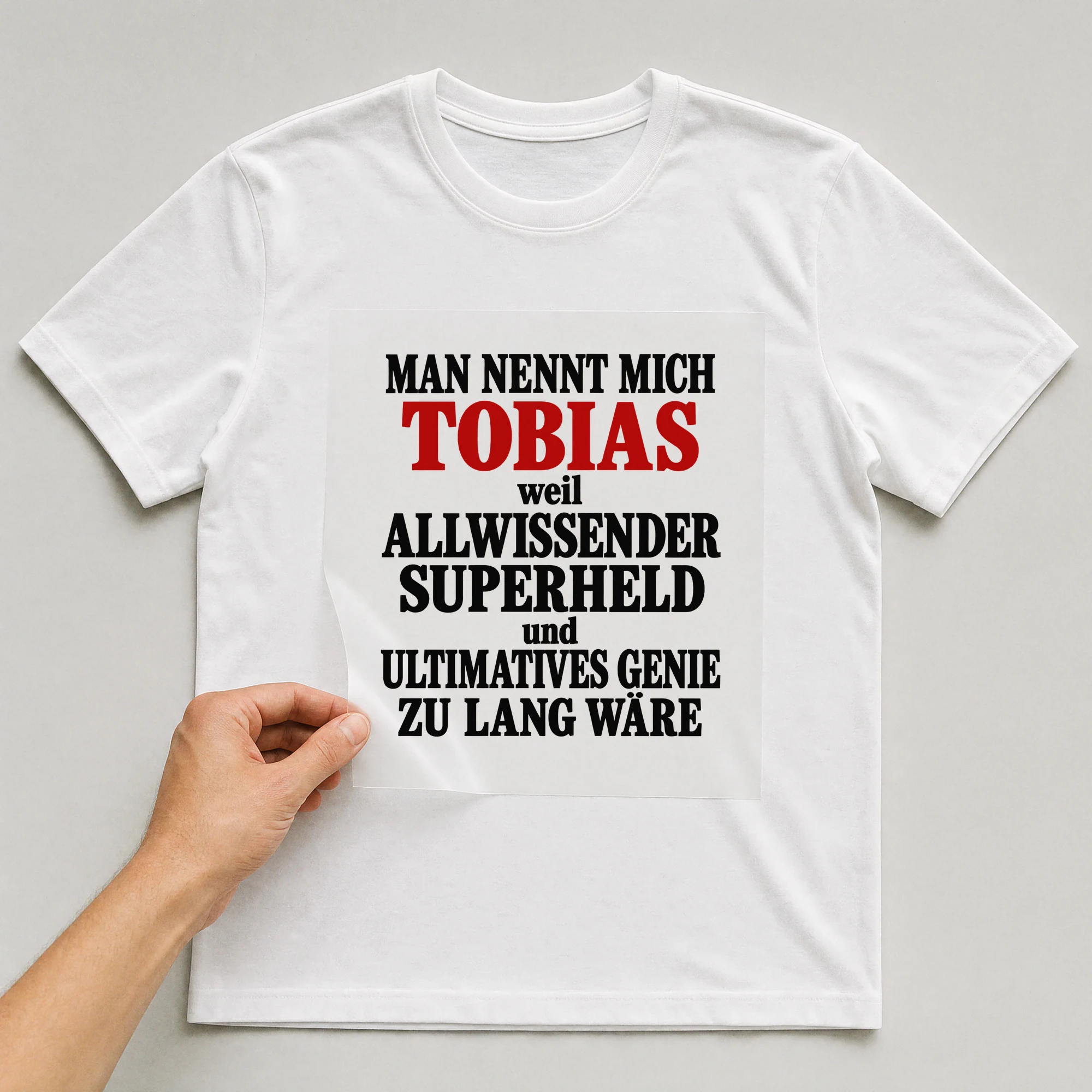 Bügelbild „Man nennt mich Tobias weil allwissender Superheld und ultimatives Genie zu“ auf weißem T-Shirt, Folie wird aufgelegt