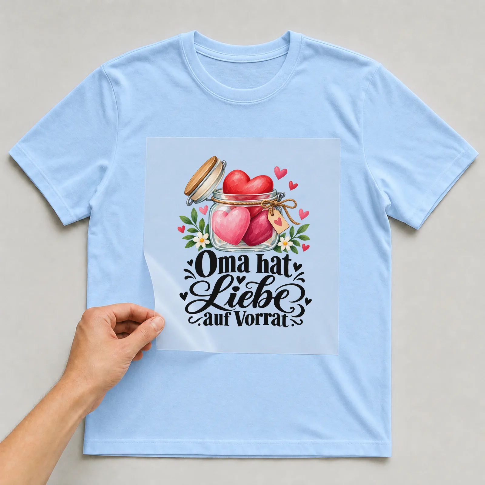 Bügelbild „Oma hat Liebe auf Vorrat“ auf hellblauem T-Shirt, Folie wird aufgelegt