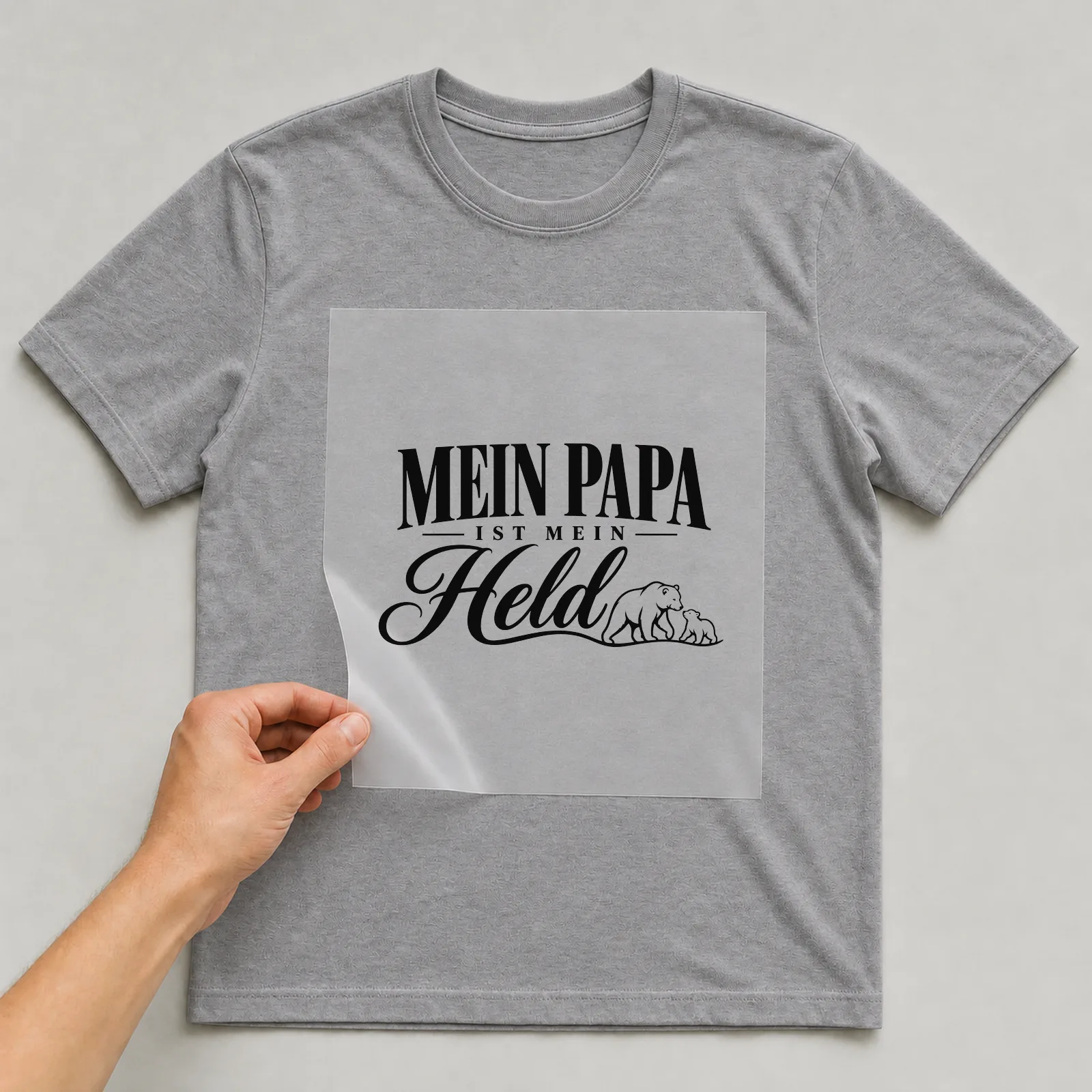 Bügelbild „Mein Papa ist mein Held“ auf grauem T-Shirt, Folie wird aufgelegt