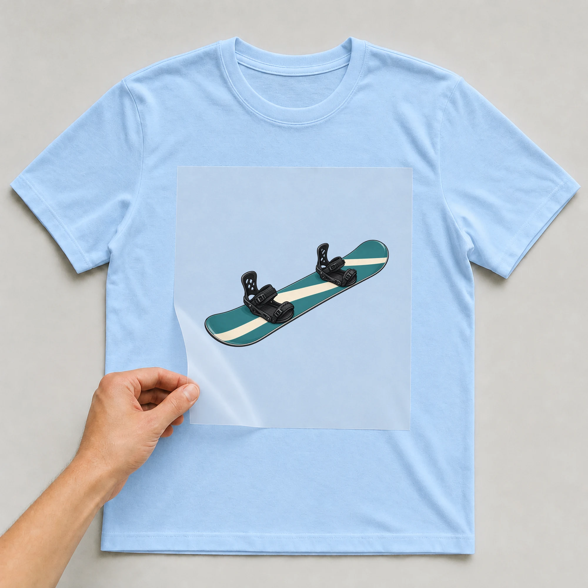 Bügelbild „Snowboard“ auf babyblauem T-Shirt, Folie wird aufgelegt