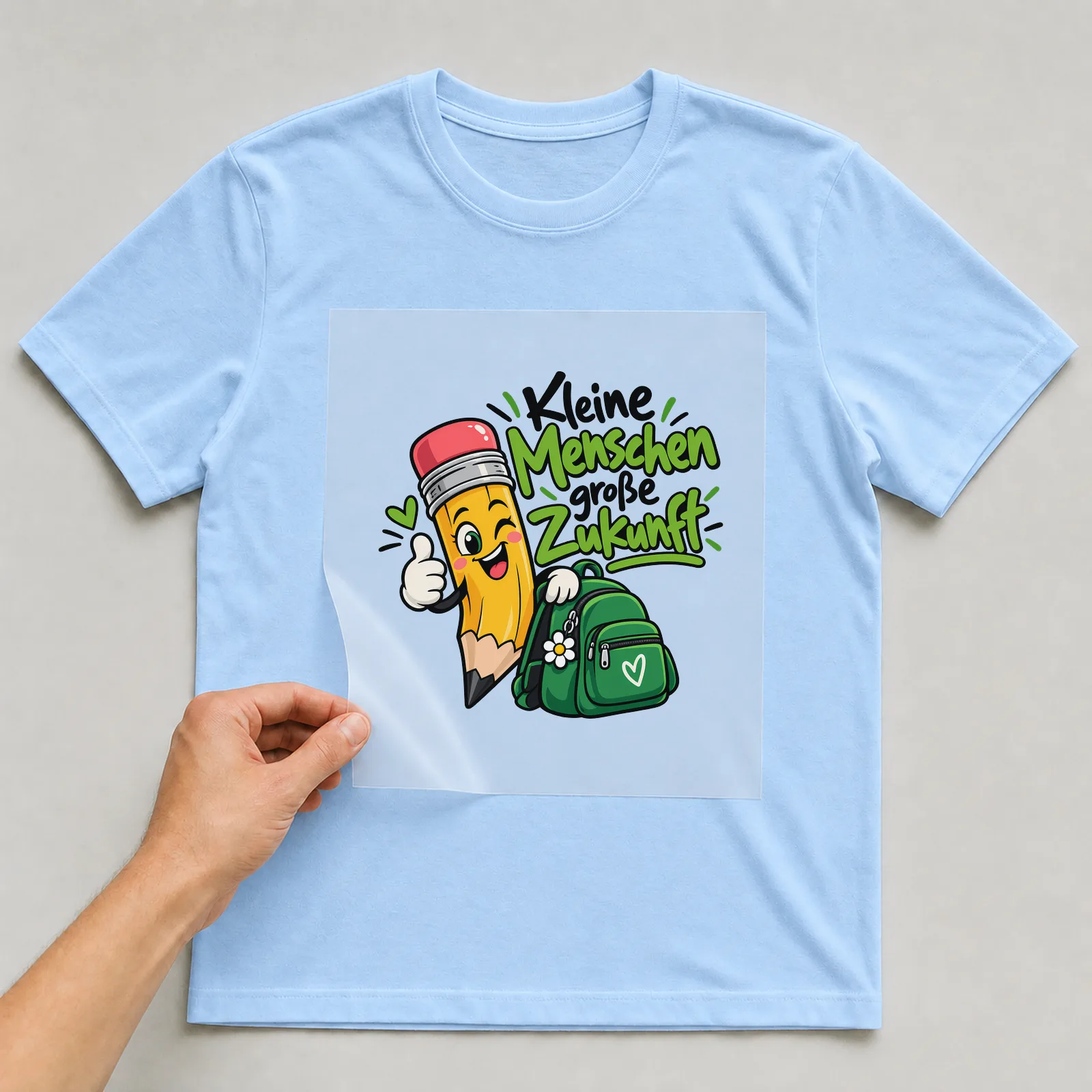 Bügelbild „Kleine Menschen große Zukunft“ auf hellblauem T-Shirt, Folie wird aufgelegt