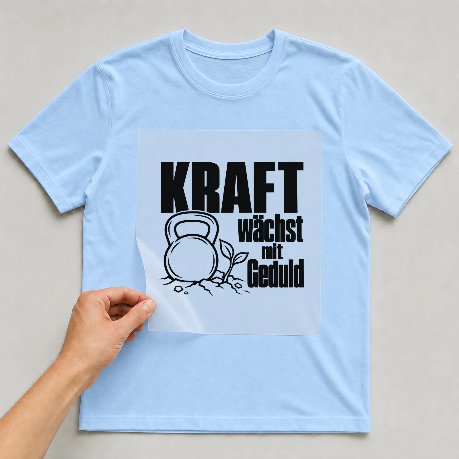 Bügelbild „Kraft wächst mit Geduld“ auf hellblauem T-Shirt, Folie wird aufgelegt