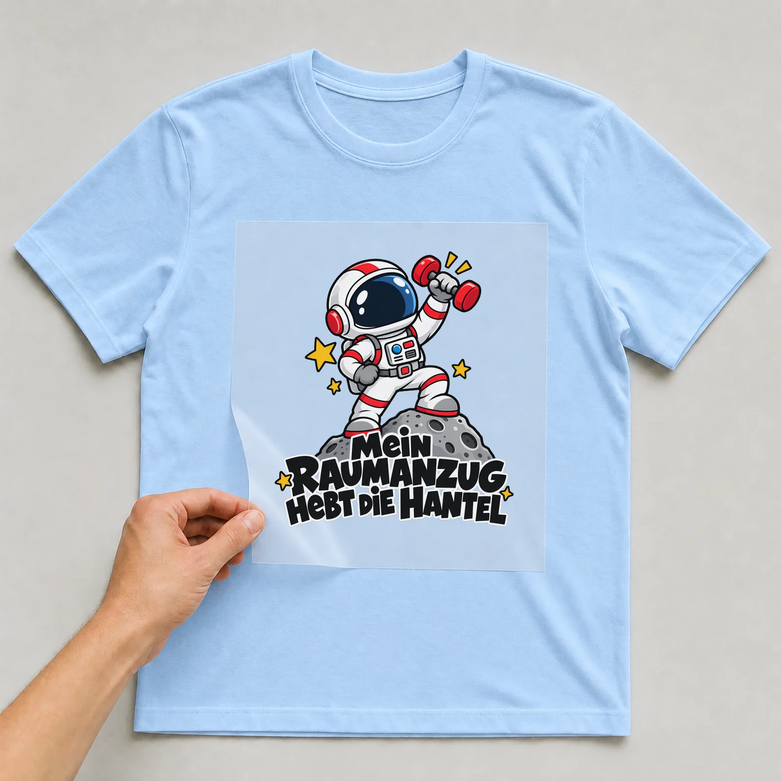 Bügelbild „Mein RAUMANZUG HEBT DIE HANTEL“ auf hellblauem T-Shirt, Folie wird aufgelegt