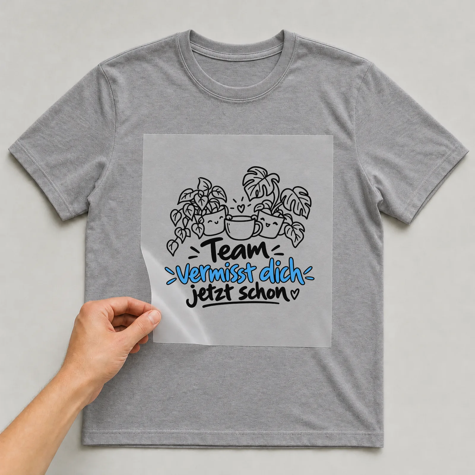 Bügelbild „Team vermisst dich jetzt schon“ auf grauem T-Shirt, Folie wird aufgelegt