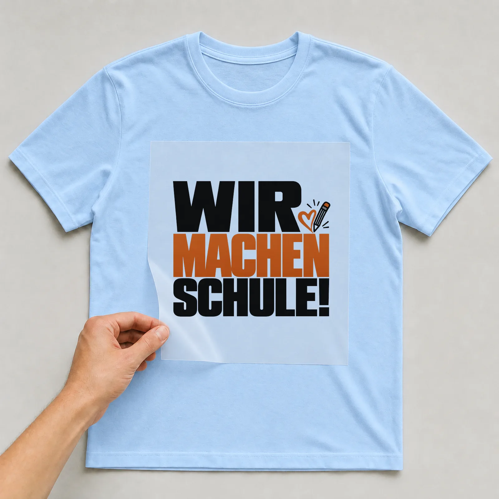Bügelbild „Wir machen Schule!“ auf hellblauem T-Shirt, Folie wird aufgelegt