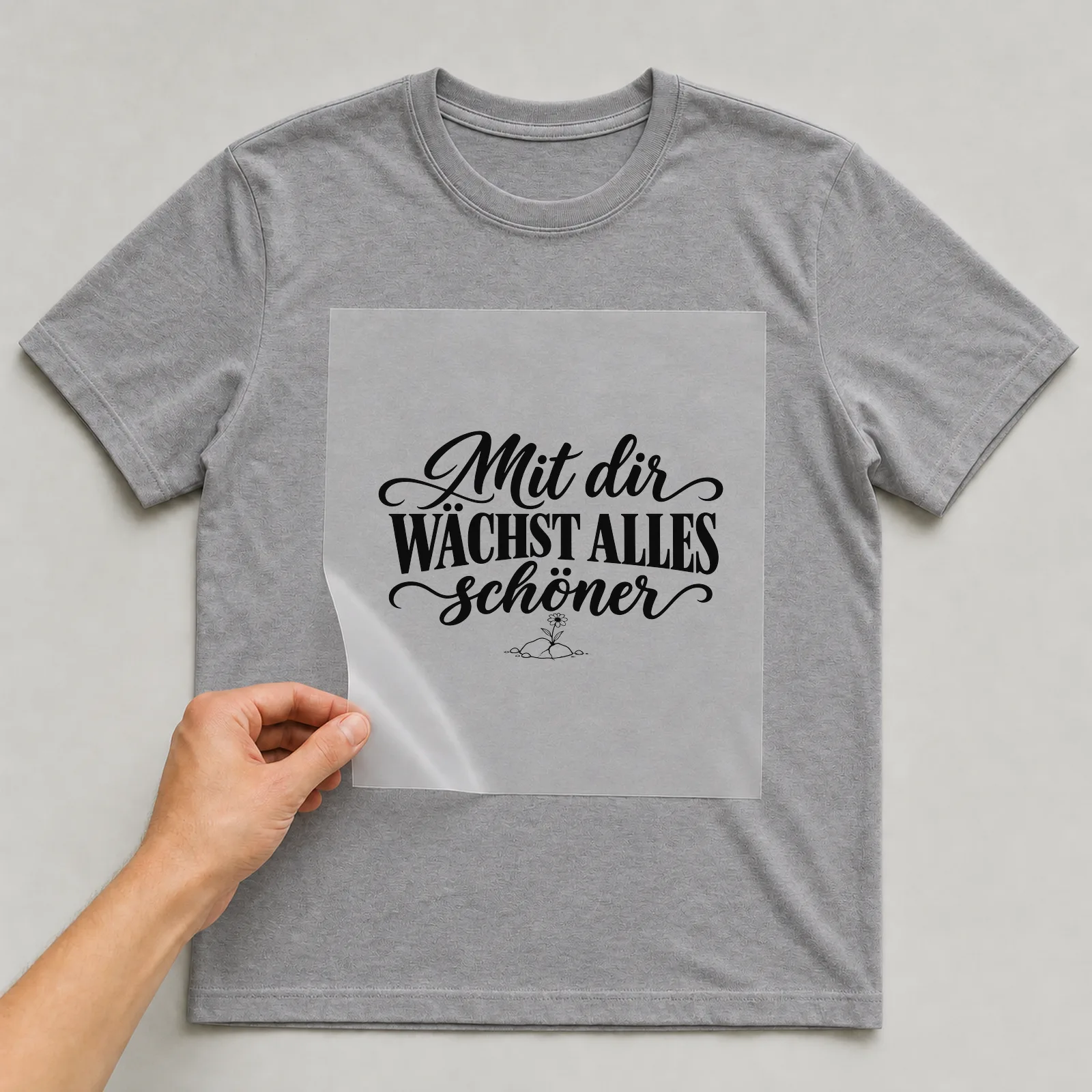 Bügelbild „Mit dir wächst alles schöner“ auf grauem T-Shirt, Folie wird aufgelegt