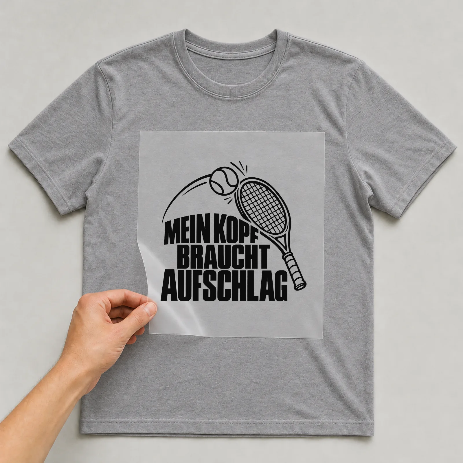 Bügelbild „Mein Kopf braucht Aufschlag“ auf grauem T-Shirt, Folie wird aufgelegt