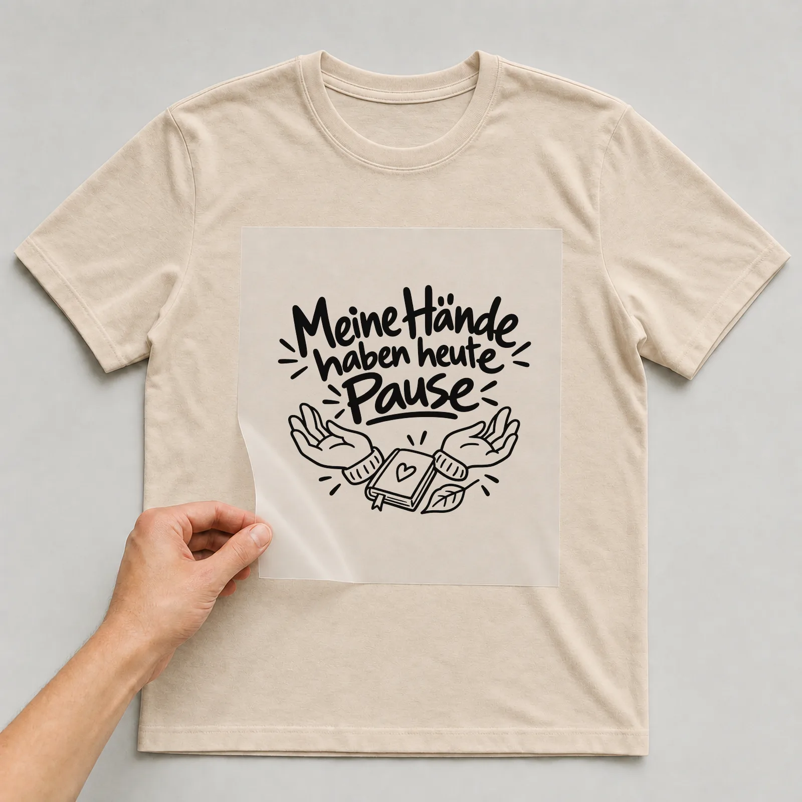 Bügelbild „Meine Hände haben heute Pause“ auf beigem T-Shirt, Folie wird aufgelegt
