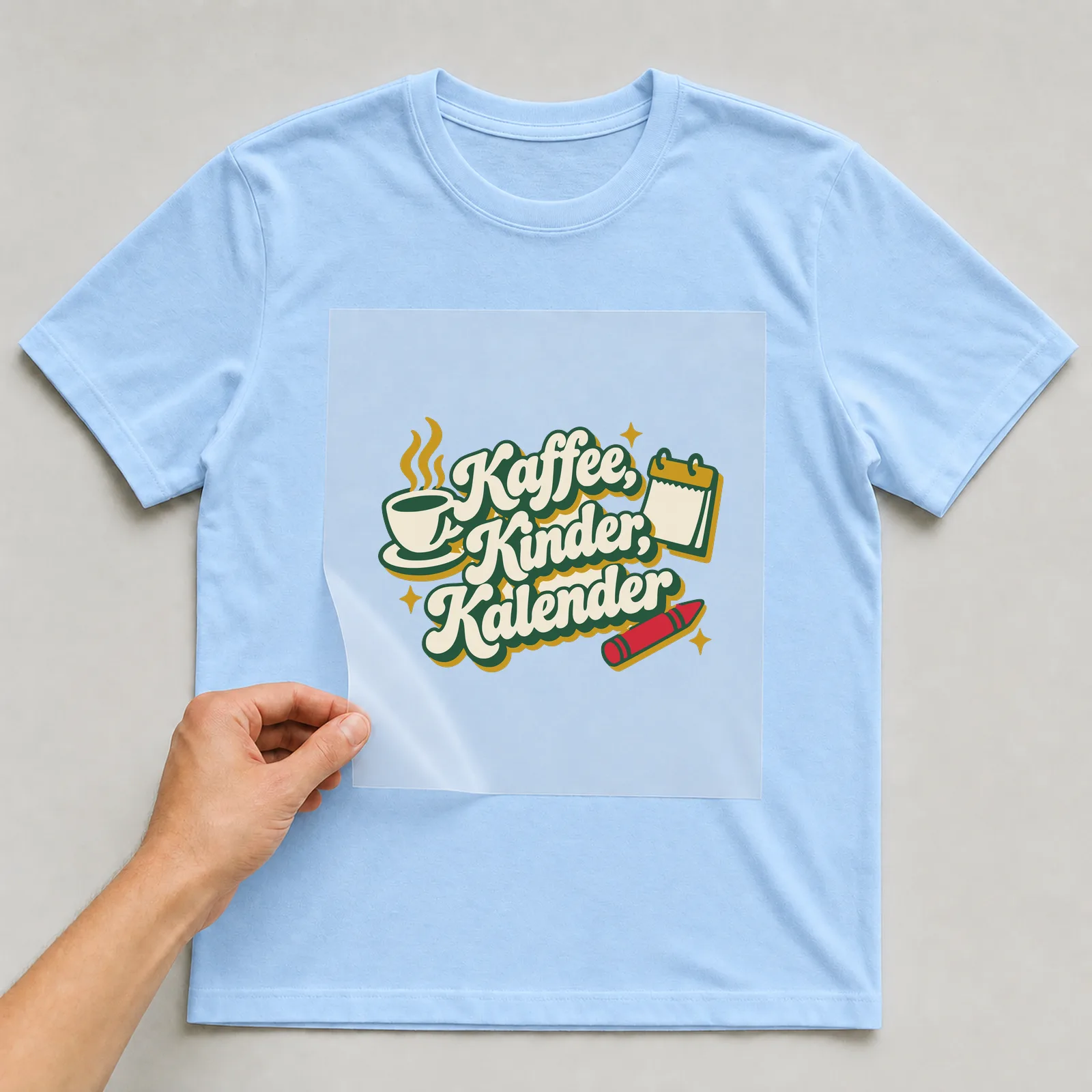 Bügelbild Kaffee, Kinder, Kalender auf hellblauem T-Shirt, Folie wird aufgelegt